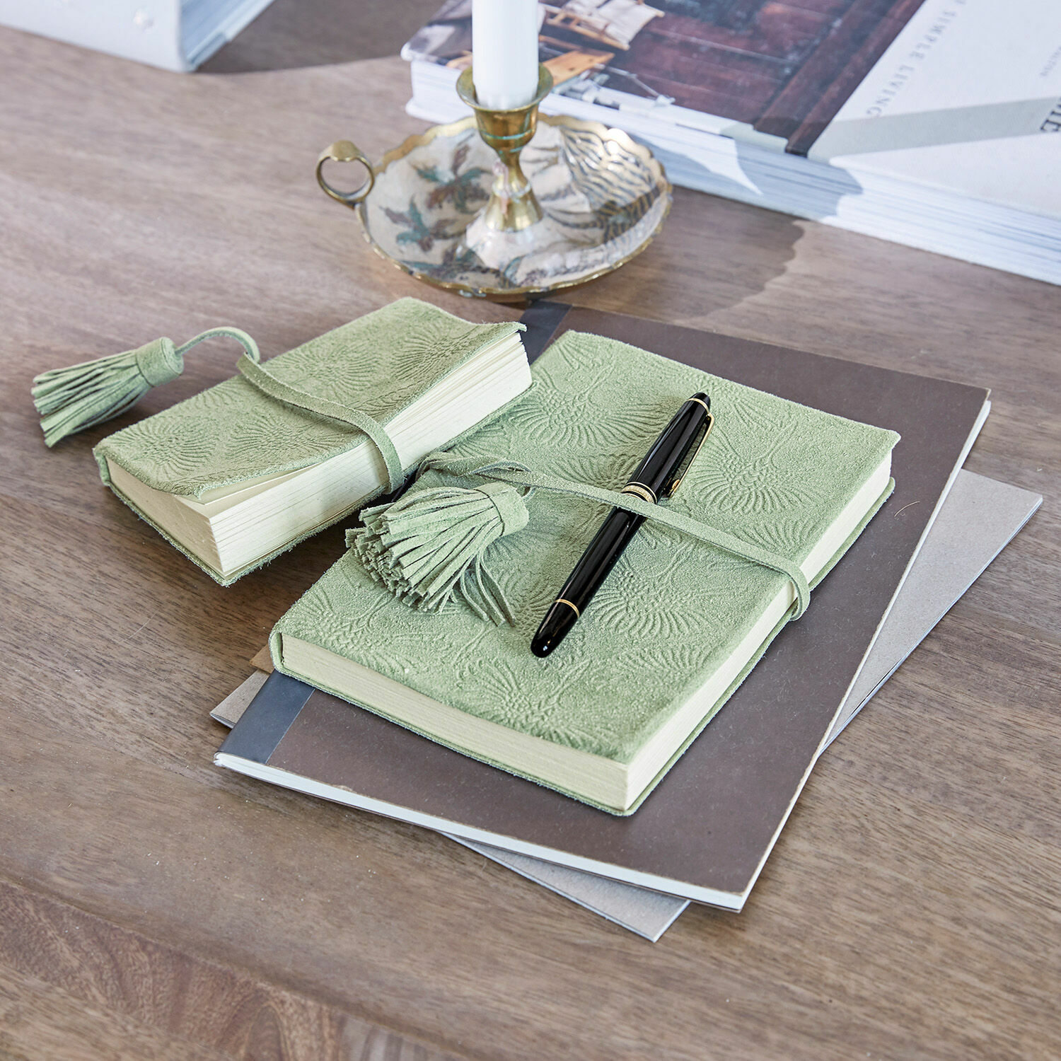 Carnet vert en cuir souple embossé avec pompons posé sur un bureau en bois avec stylo noir