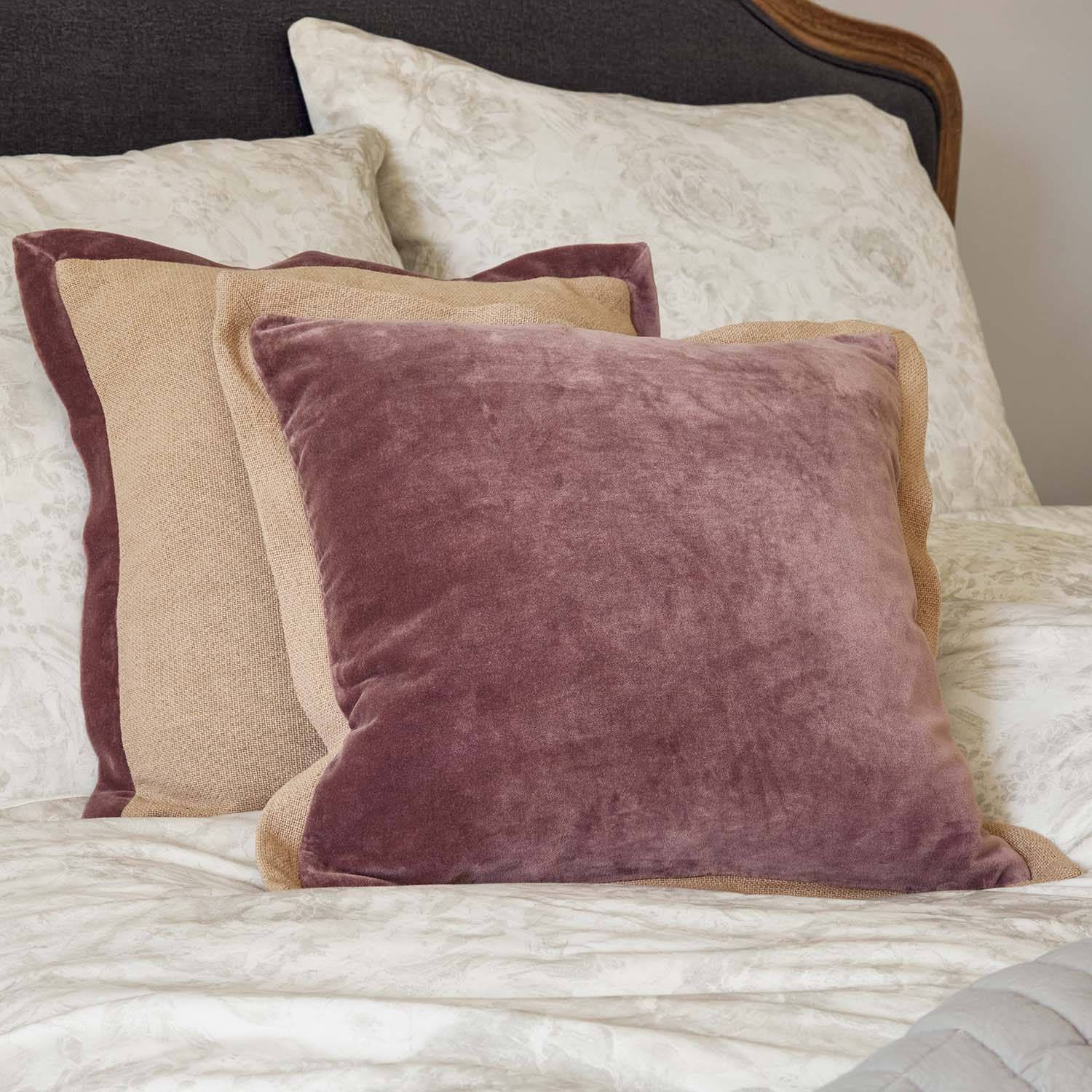 Ensemble de coussins décoratifs en velours et lin rose et beige sur un lit à motifs floraux
