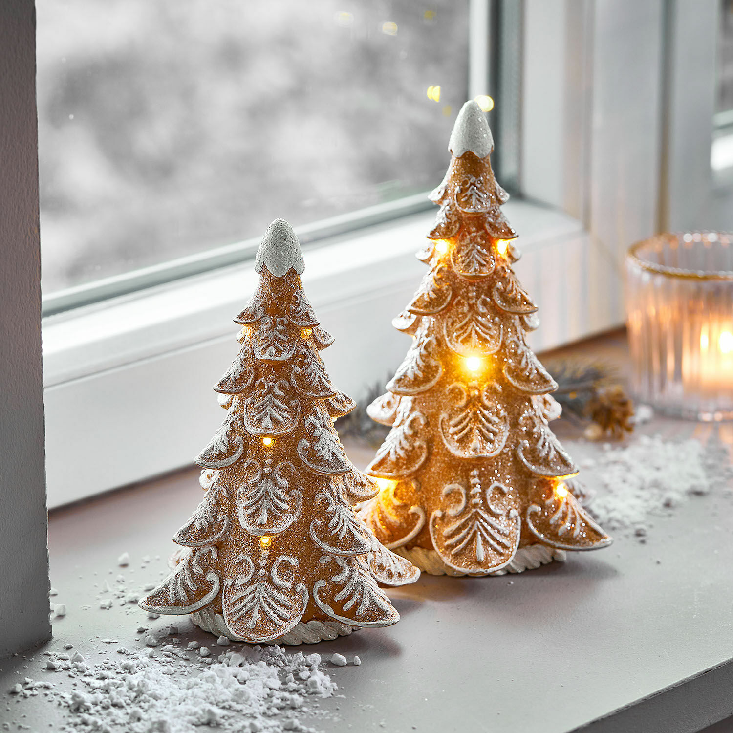 Deux sapins décoratifs en céramique avec éclairage LED et effet neige blanche sur le rebord de fenêtre