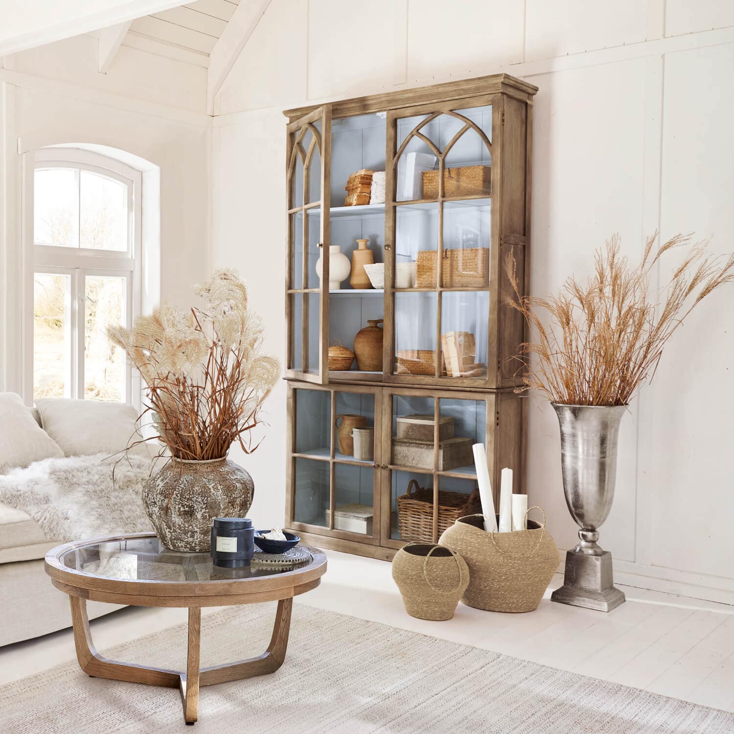 Gezellige woonkamer met houten vitrinekast, glazen tafel en natuurlijke decoraties in lichte kleuren