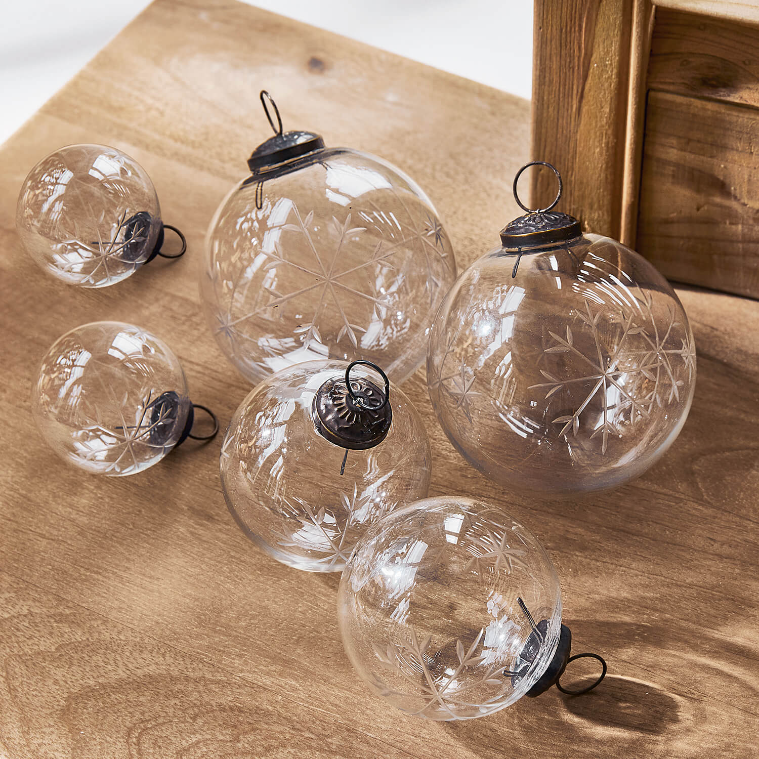 Boules de Noël en verre transparent avec motif flocon gravé posées sur une table en bois, décoration festive