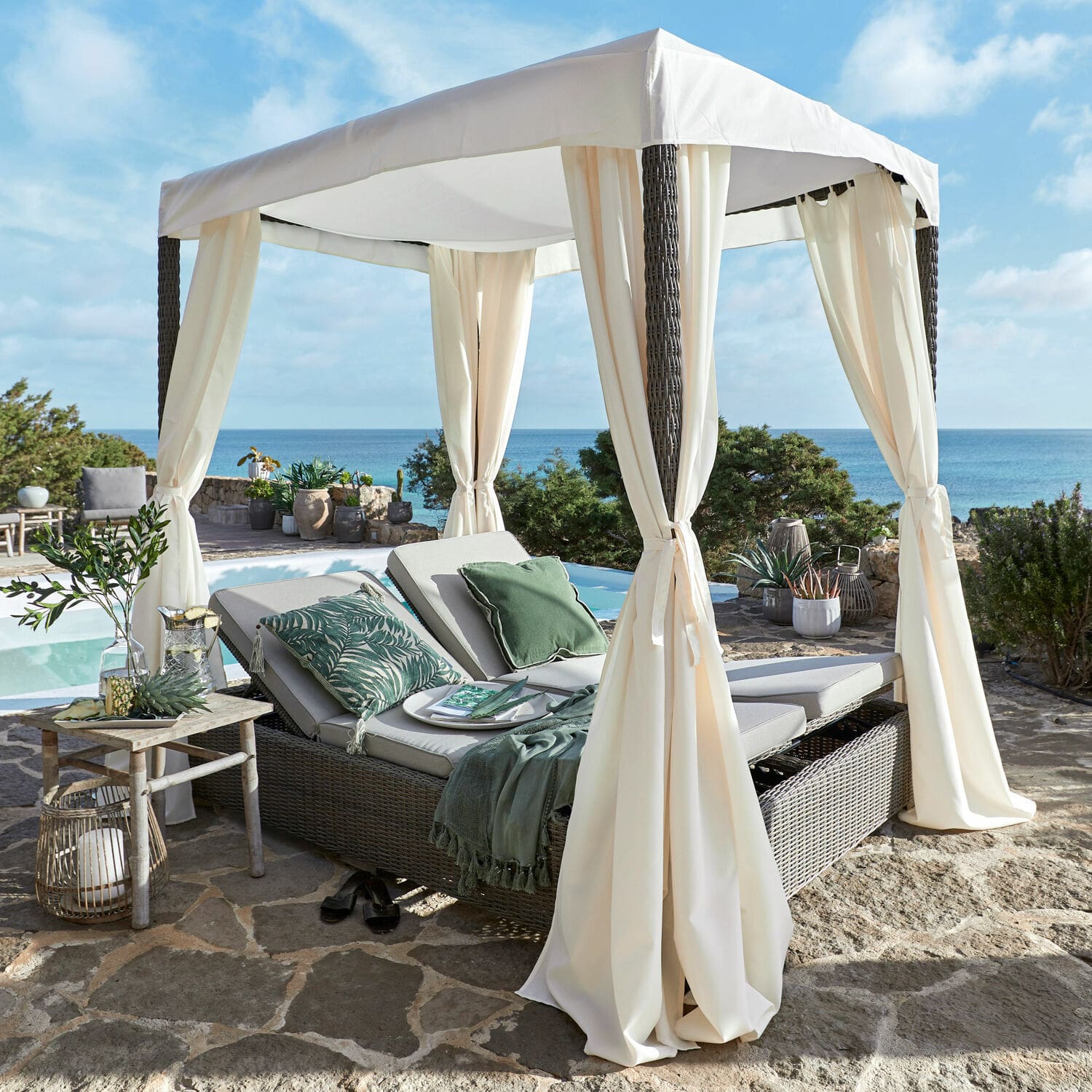 Chaise longue de jardin en rotin avec auvent crème sur terrasse en pierre face à la mer