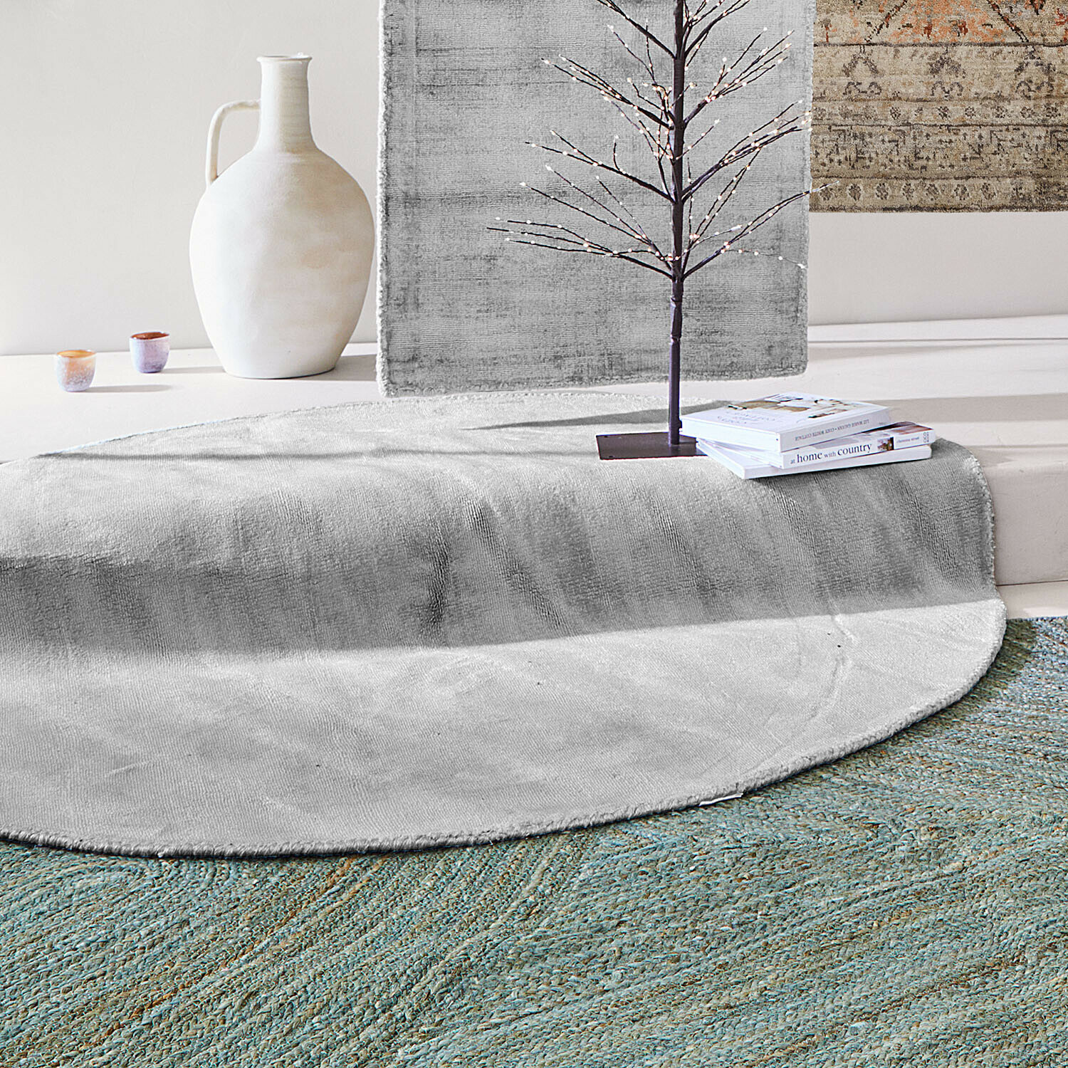 Vloerkleed Mariselle Ronde grijze vloerkleed van zacht materiaal met decoratieve vaas en boeken in een moderne ruimte
