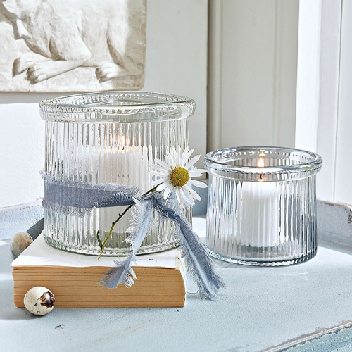 Glazen windlichten van geribbeld glas met witte kaarsen en decoratief lint met bloem.
