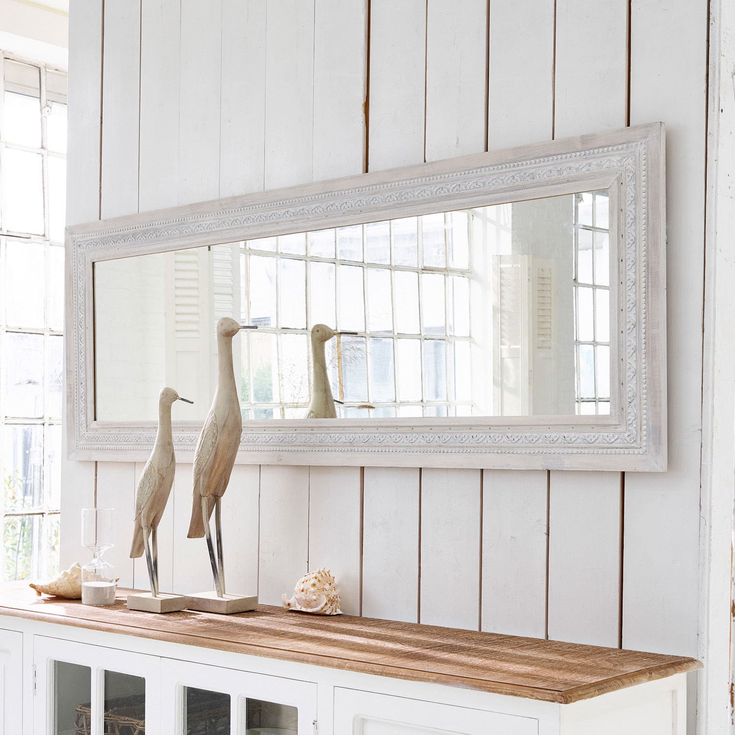 Miroir Milanu Grand miroir rectangulaire avec cadre en bois blanc au-dessus d'un buffet blanc décoré de sculptures en bois et coquillages