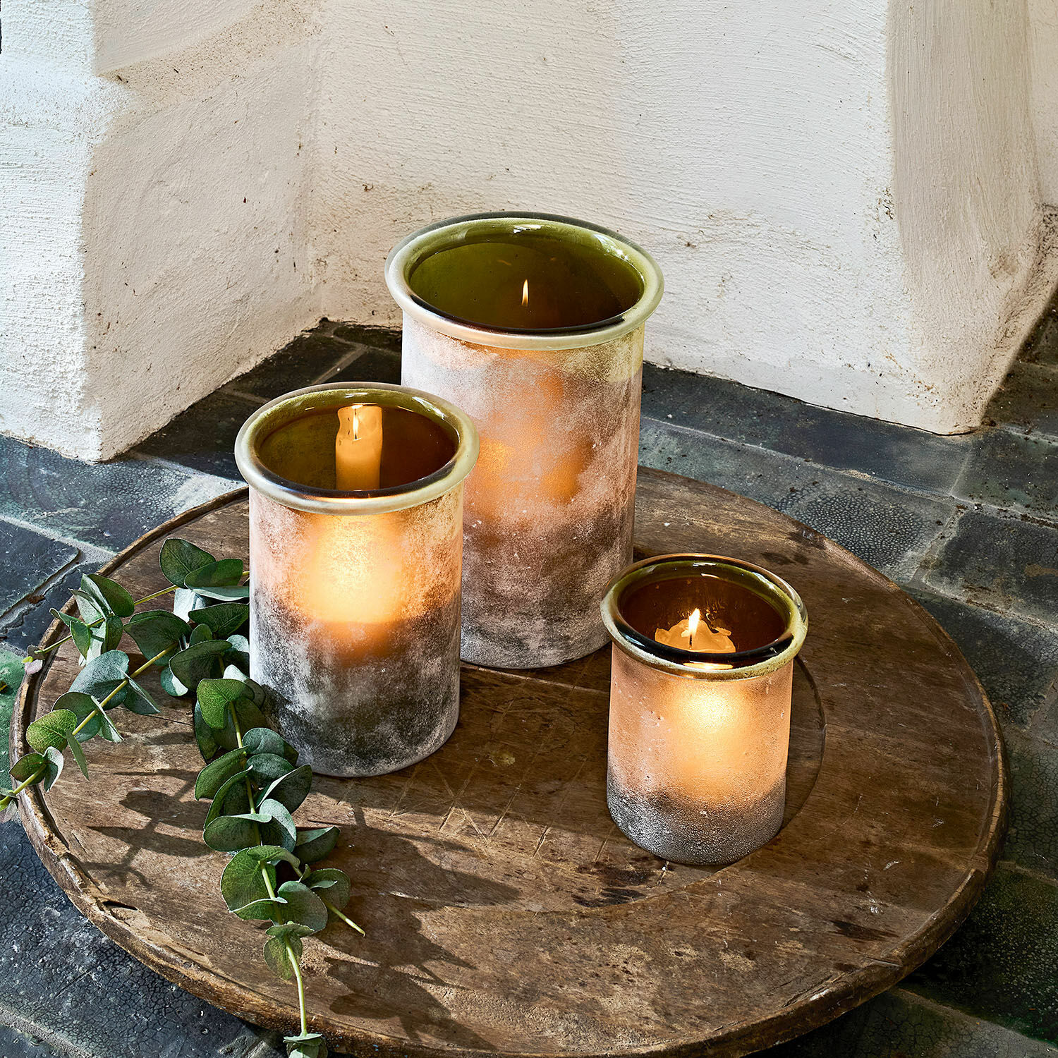 Lot de 3 photophores Iskira Ensemble de trois photophores en verre mat brun et vert posés sur un plateau en bois rustique