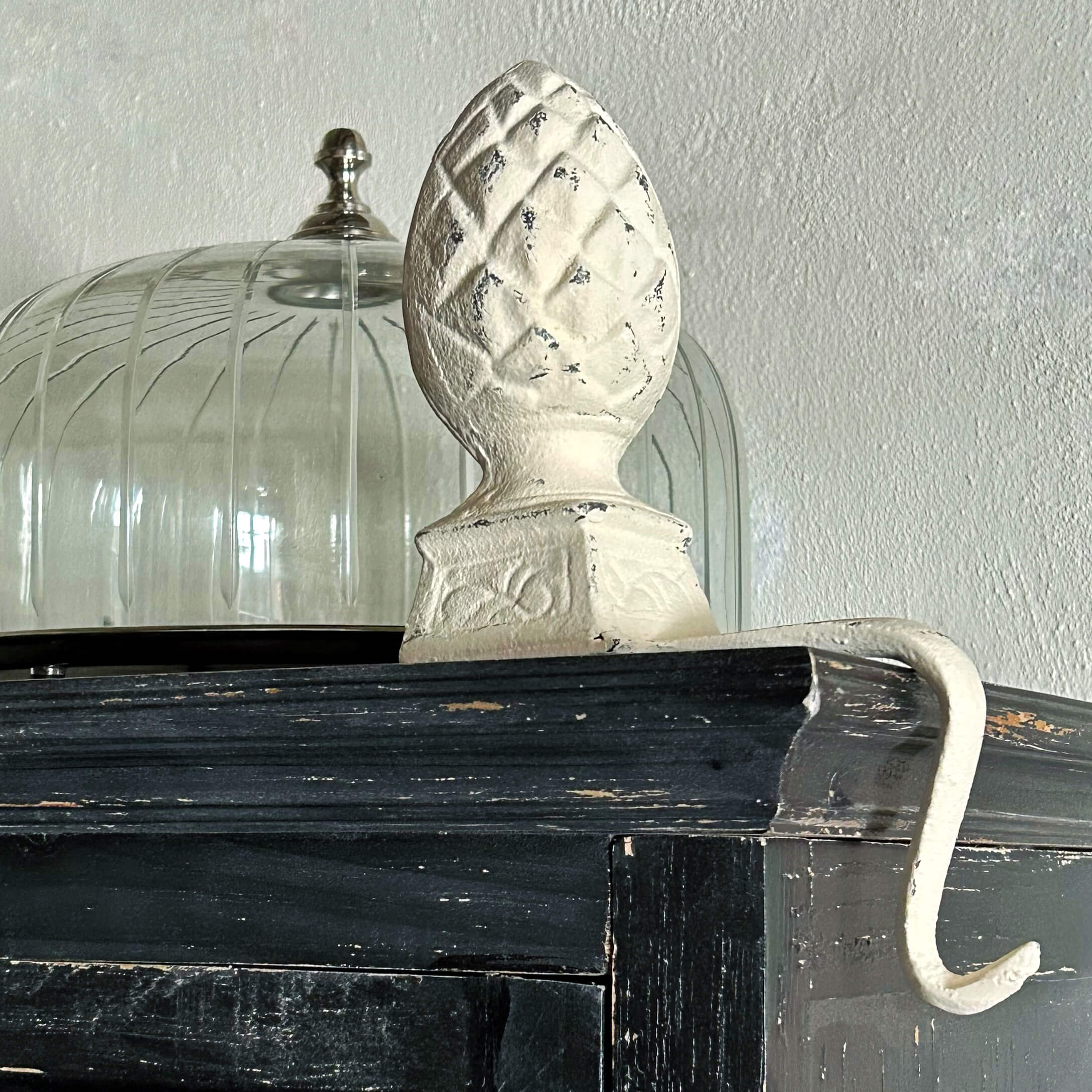 Witte metalen haak met decoratieve dennenappelvormige top op zwarte houten plank
