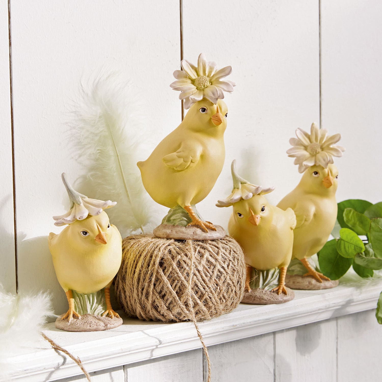 Quatre figurines de poussins jaunes en céramique avec chapeaux floraux sur une étagère blanche décorative