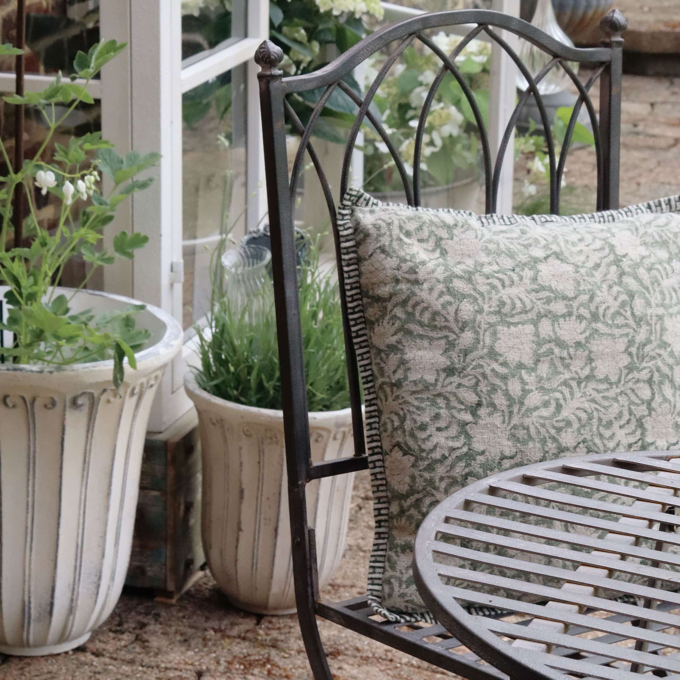 Fauteuil de jardin en métal avec coussin vert et beige, entouré de pots de fleurs décoratifs
