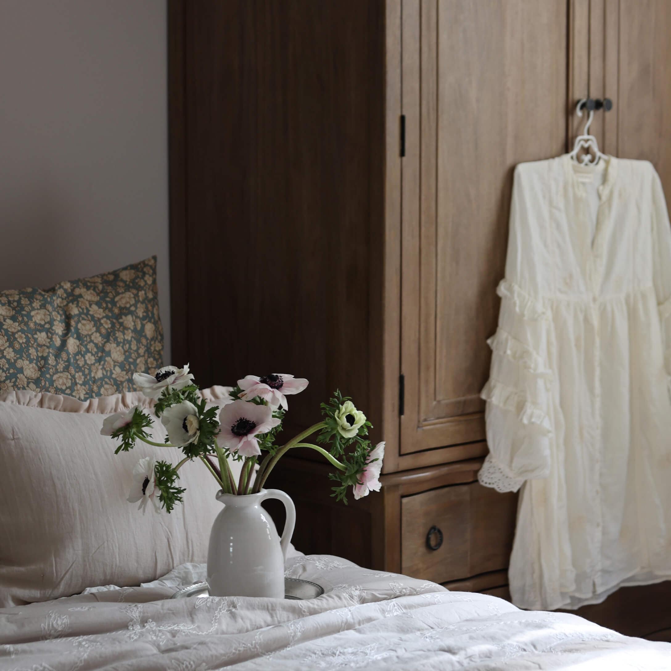 Witte keramische kan met bloemen op licht beddengoed voor een houten kast in slaapkamer