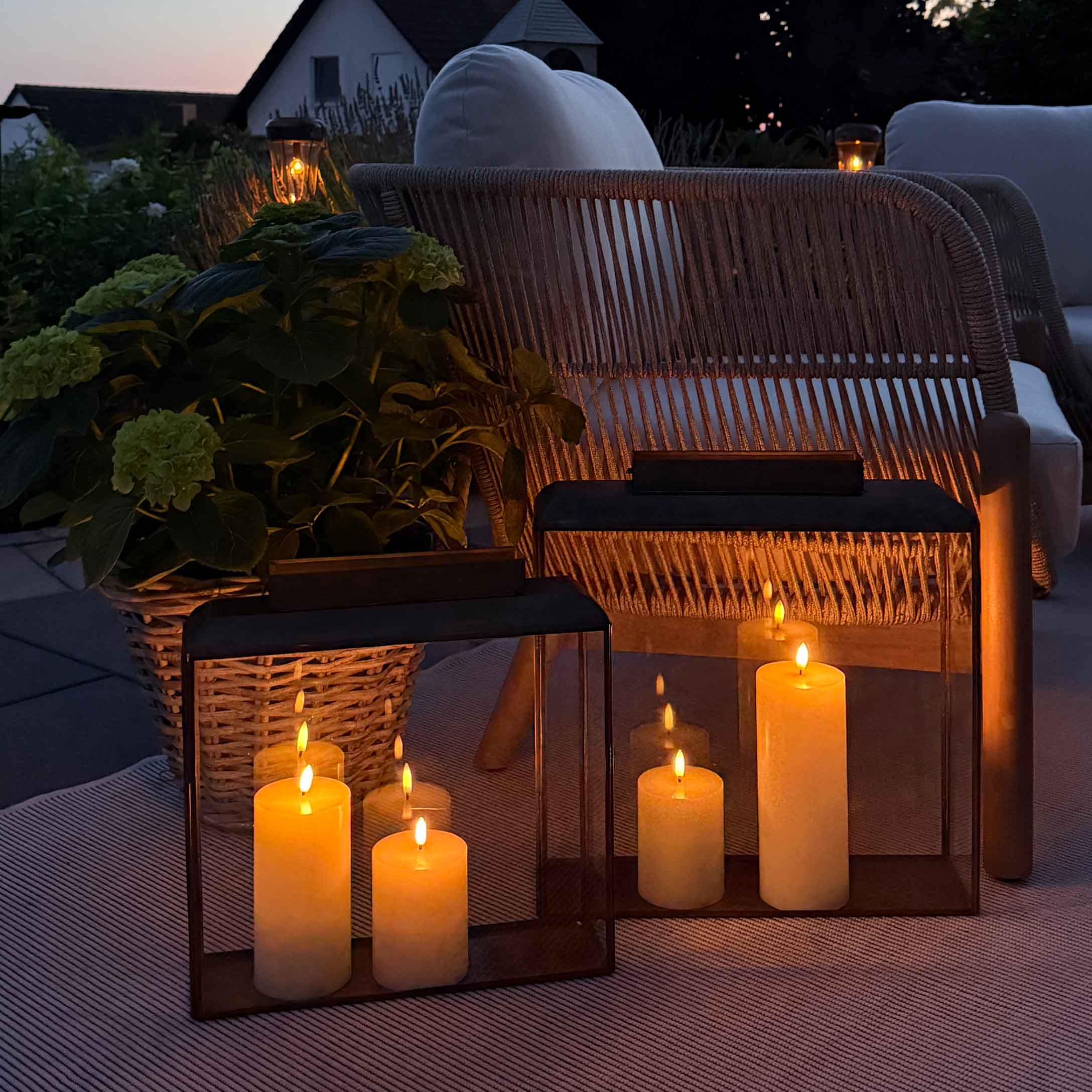 Éclairage d'ambiance avec lanternes et bougies sur terrasse avec fauteuil en osier et coussin blanc