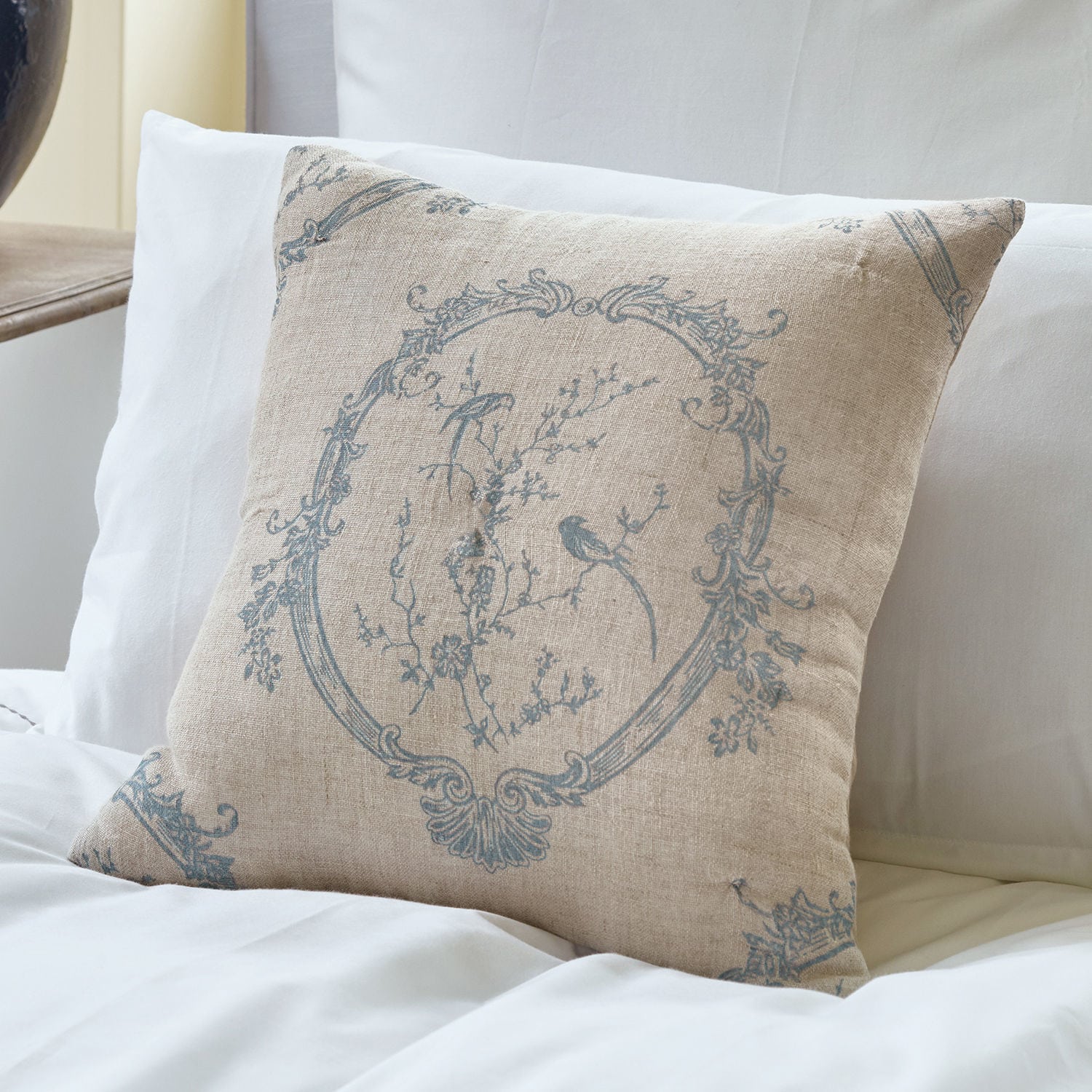 Beige linnen kussen met blauw patroon van vogels en bloemen op wit beddengoed, slaapkamerdecoratie