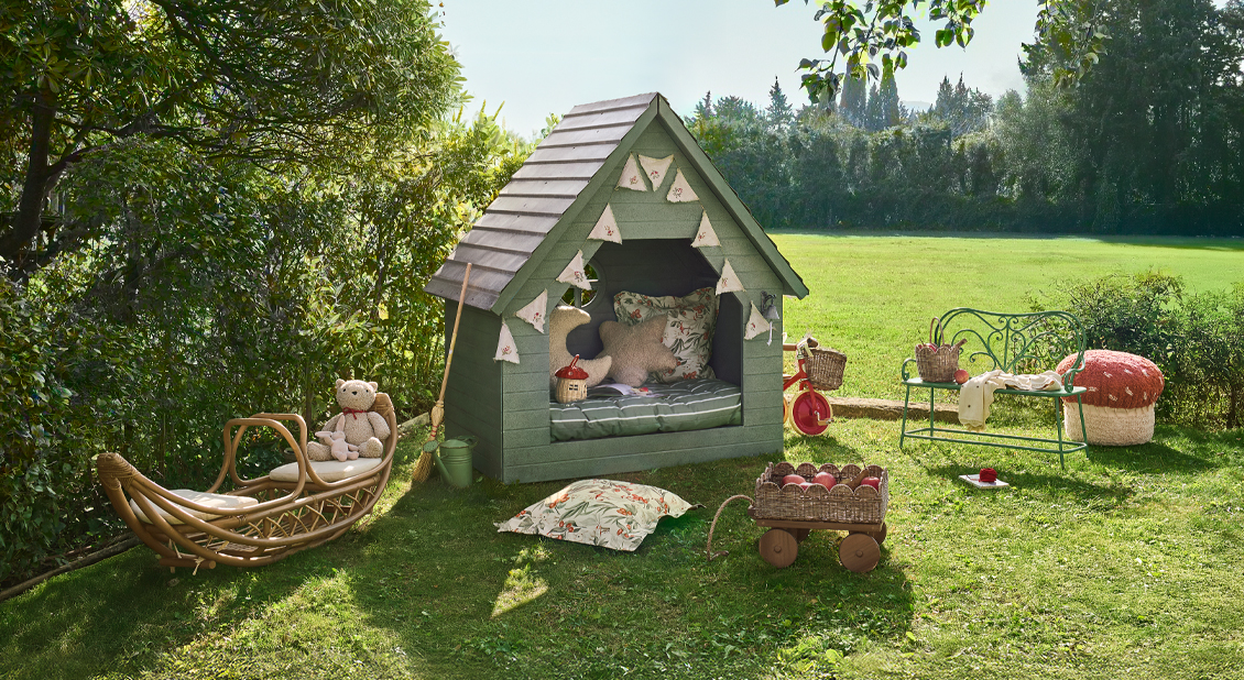 Maisonnette en bois verte avec coussins et jouets dans un jardin ensoleillé