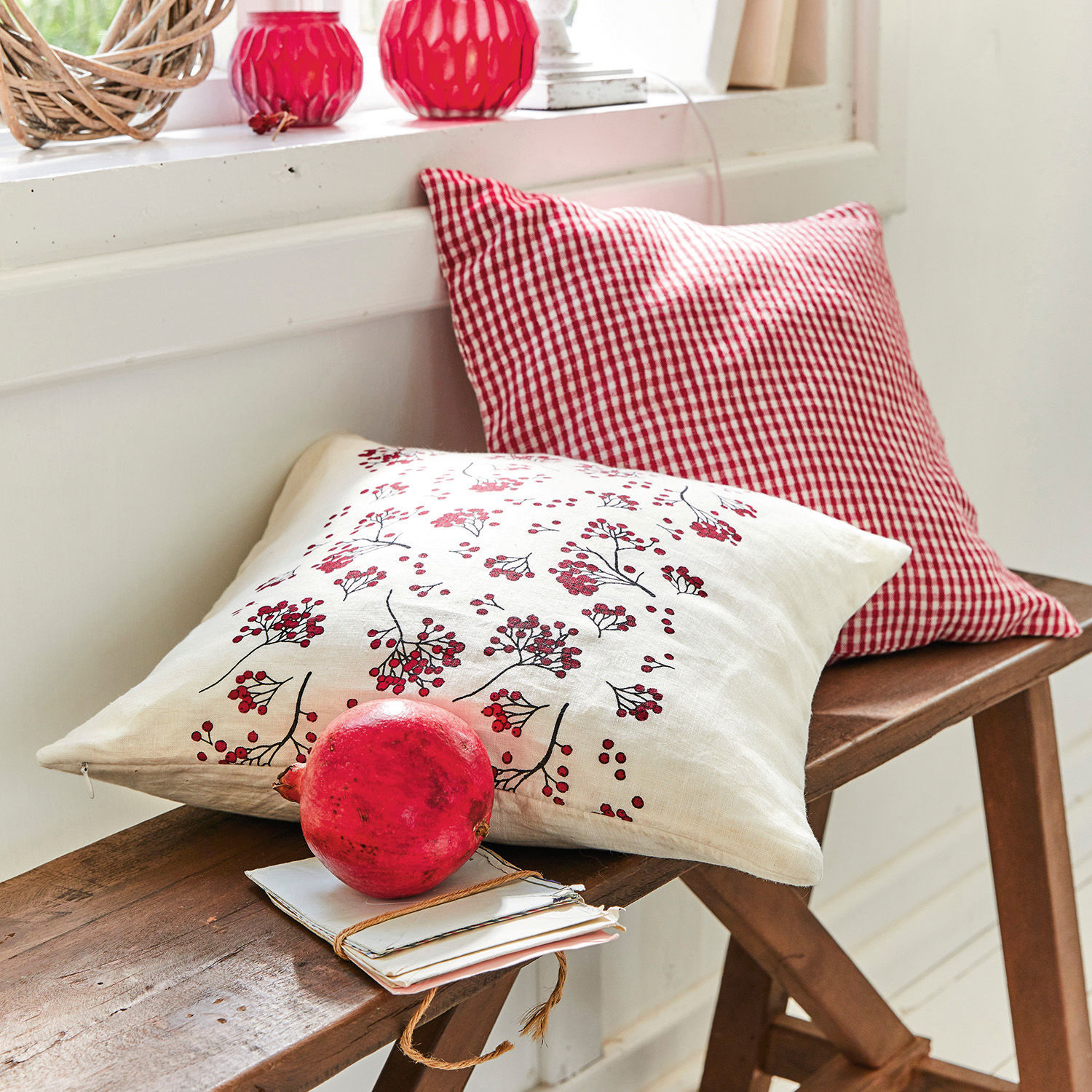 Deux coussins décoratifs en lin rouge à motifs et à carreaux sur un banc en bois avec grenade et lettres