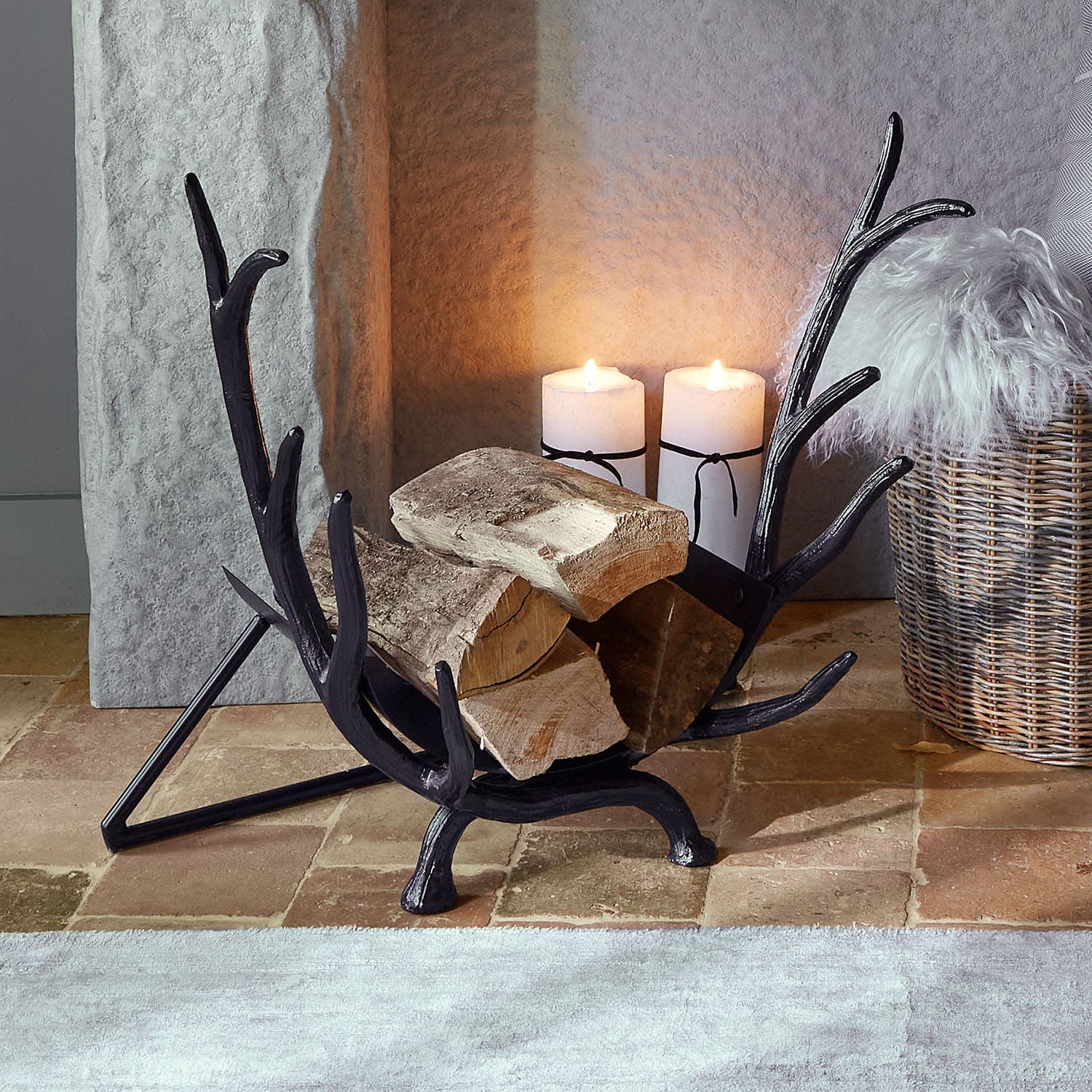 Porte-bûches en métal noir en forme de bois de cerf avec bûches et bougies allumées à côté