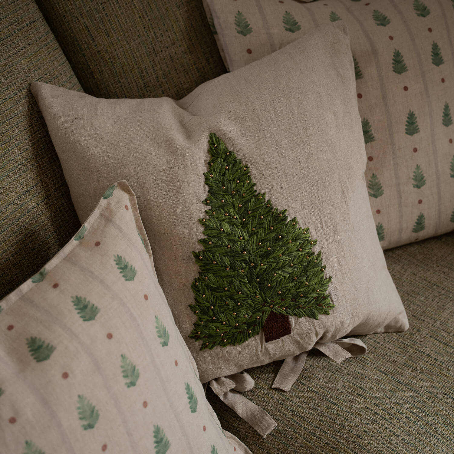 Coussin beige en lin avec arbre vert brodé et perles dorées sur canapé texturé
