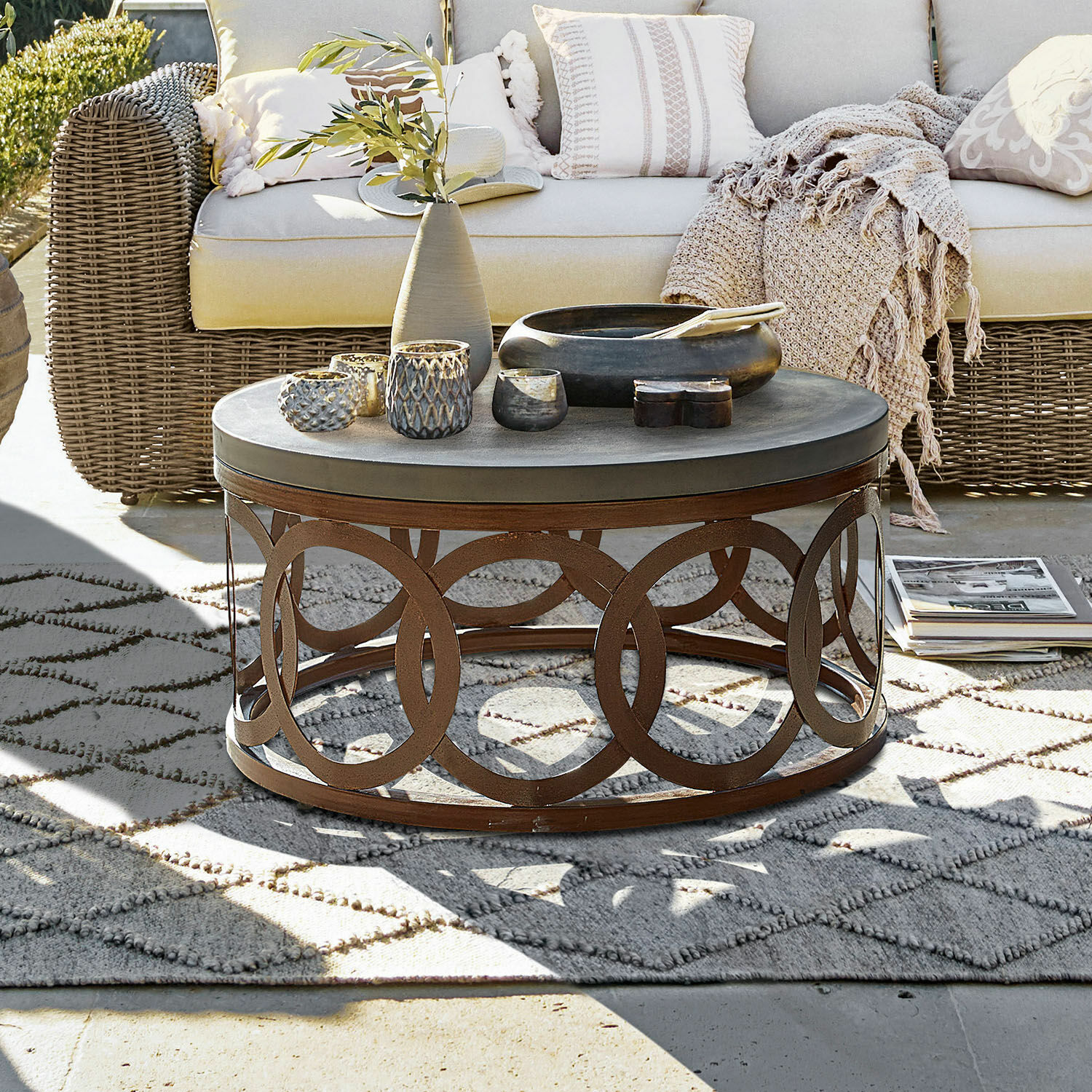 Table basse Boécourt Table basse ronde avec base en métal rouillé et plateau gris sur terrasse avec canapé en osier beige
