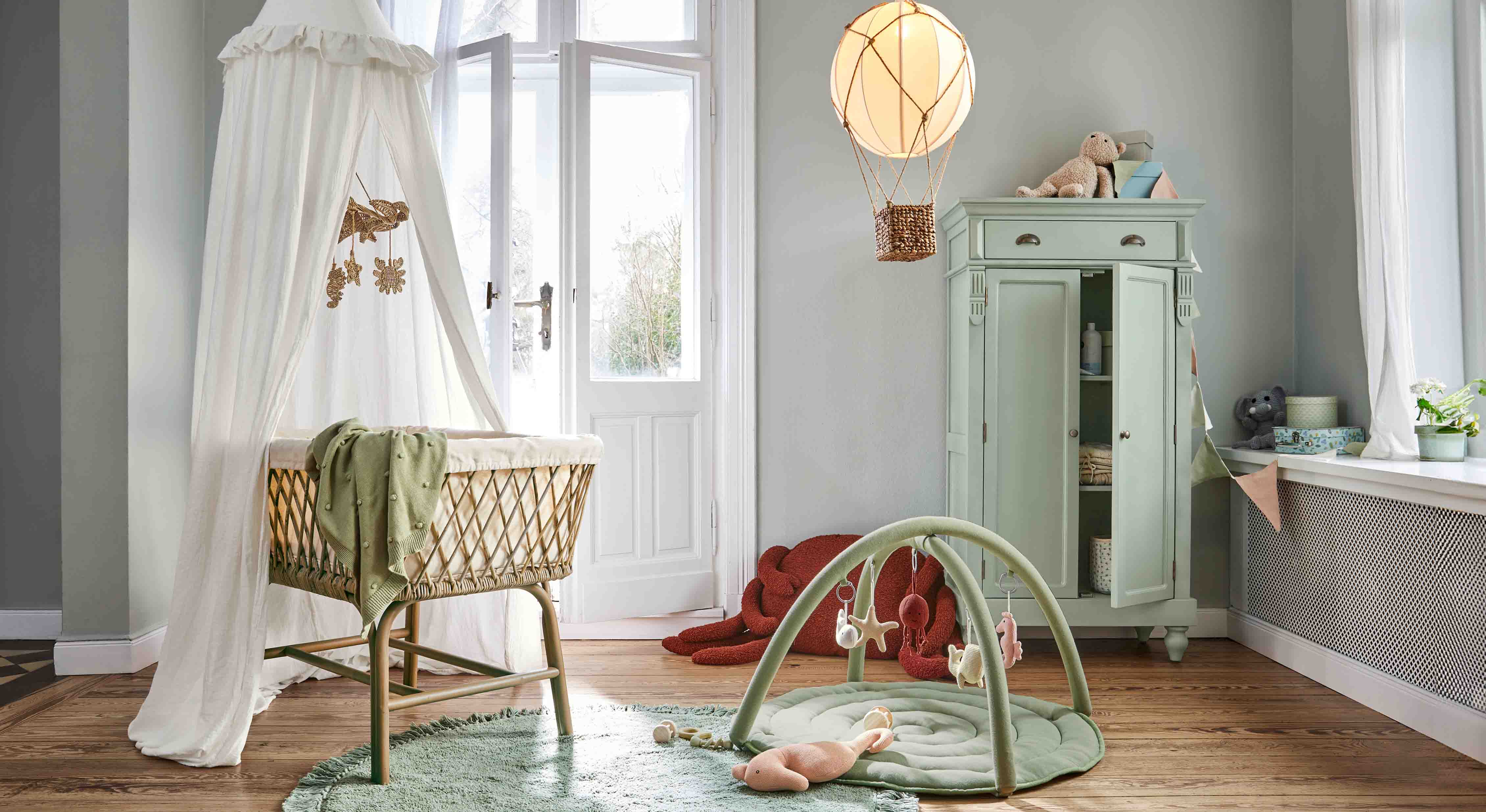 Gezellige kinderkamer met rieten wieg, groene vloerkleed en pastel kast voor speelgoed en opbergruimte