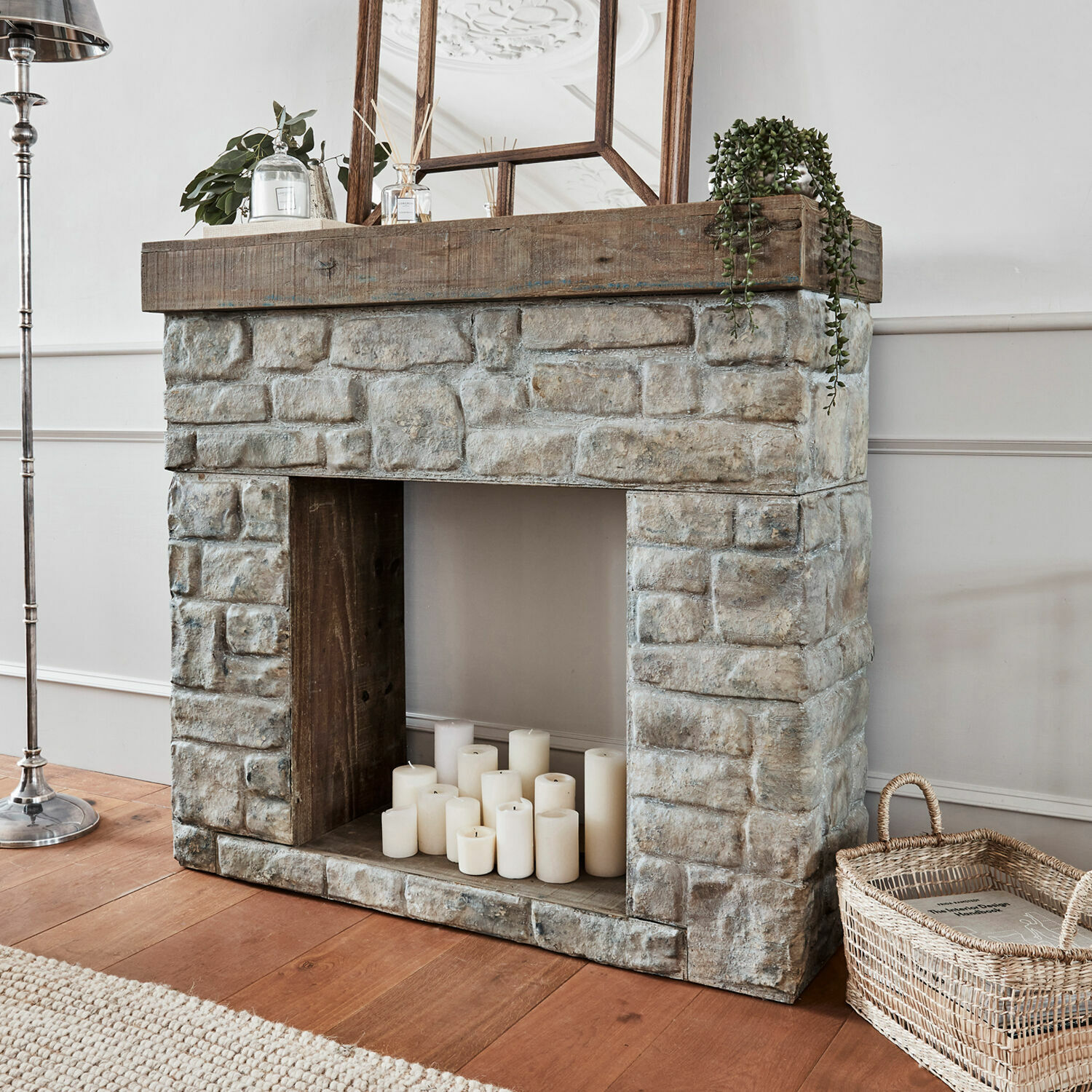 Haardschouw Evreux Decoratieve open haard van grijs steen en hout met witte kaarsen en rieten mand