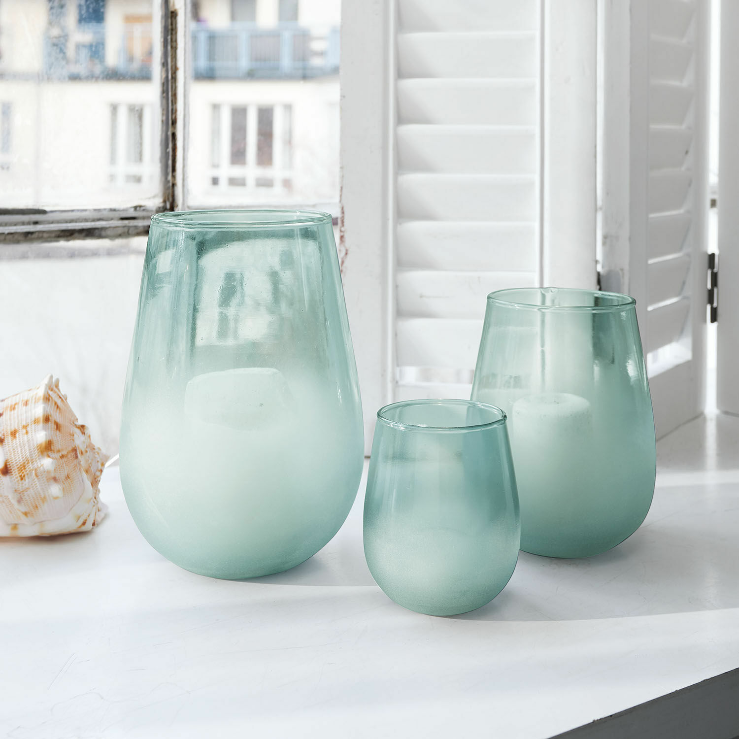 Lot de 3 photophores Miristelle Ensemble de trois photophores en verre dépoli vert clair posés sur un rebord de fenêtre blanc