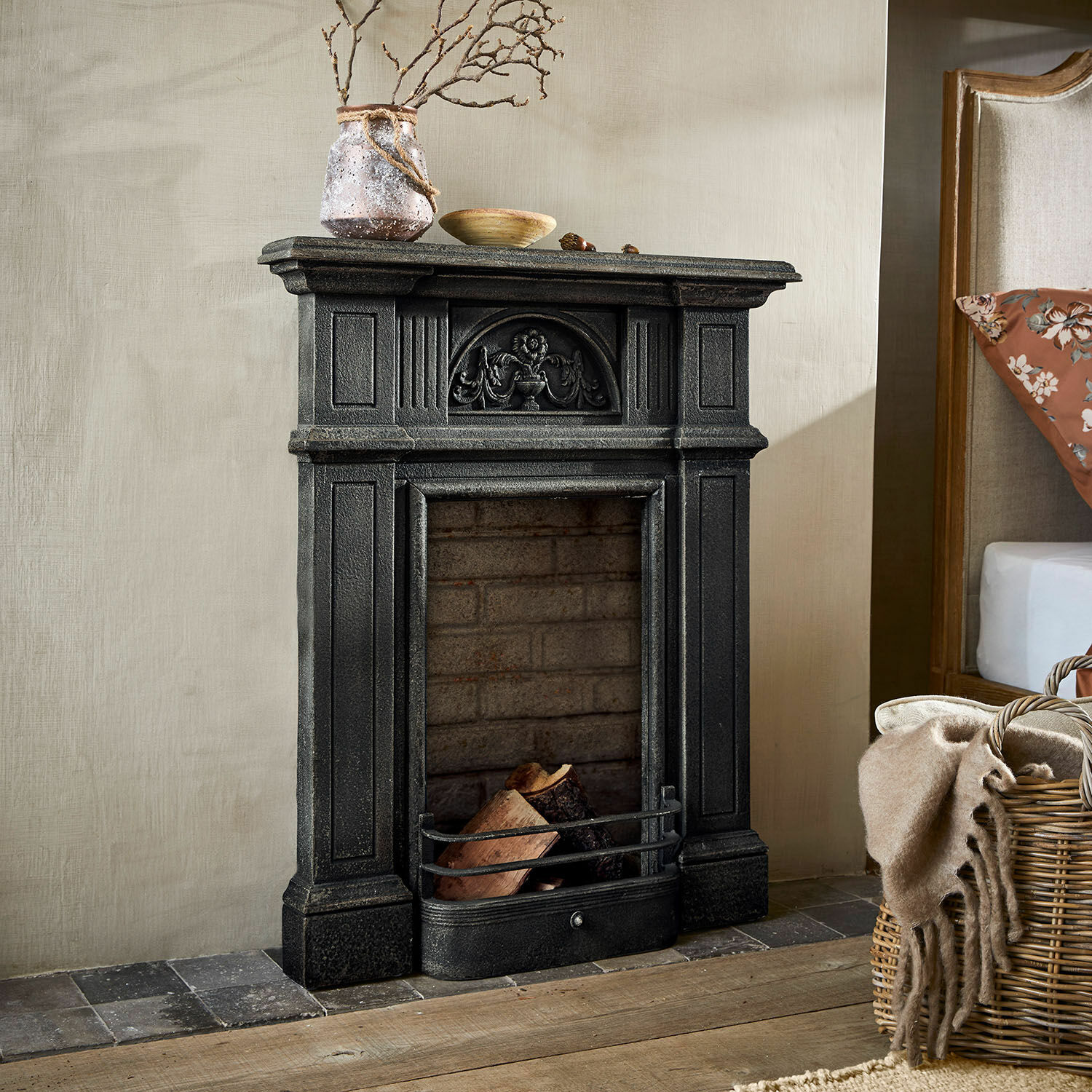 Haardschouw Corvelle Zwarte decoratieve gietijzeren open haard met hout en versieringen in rustieke kamer