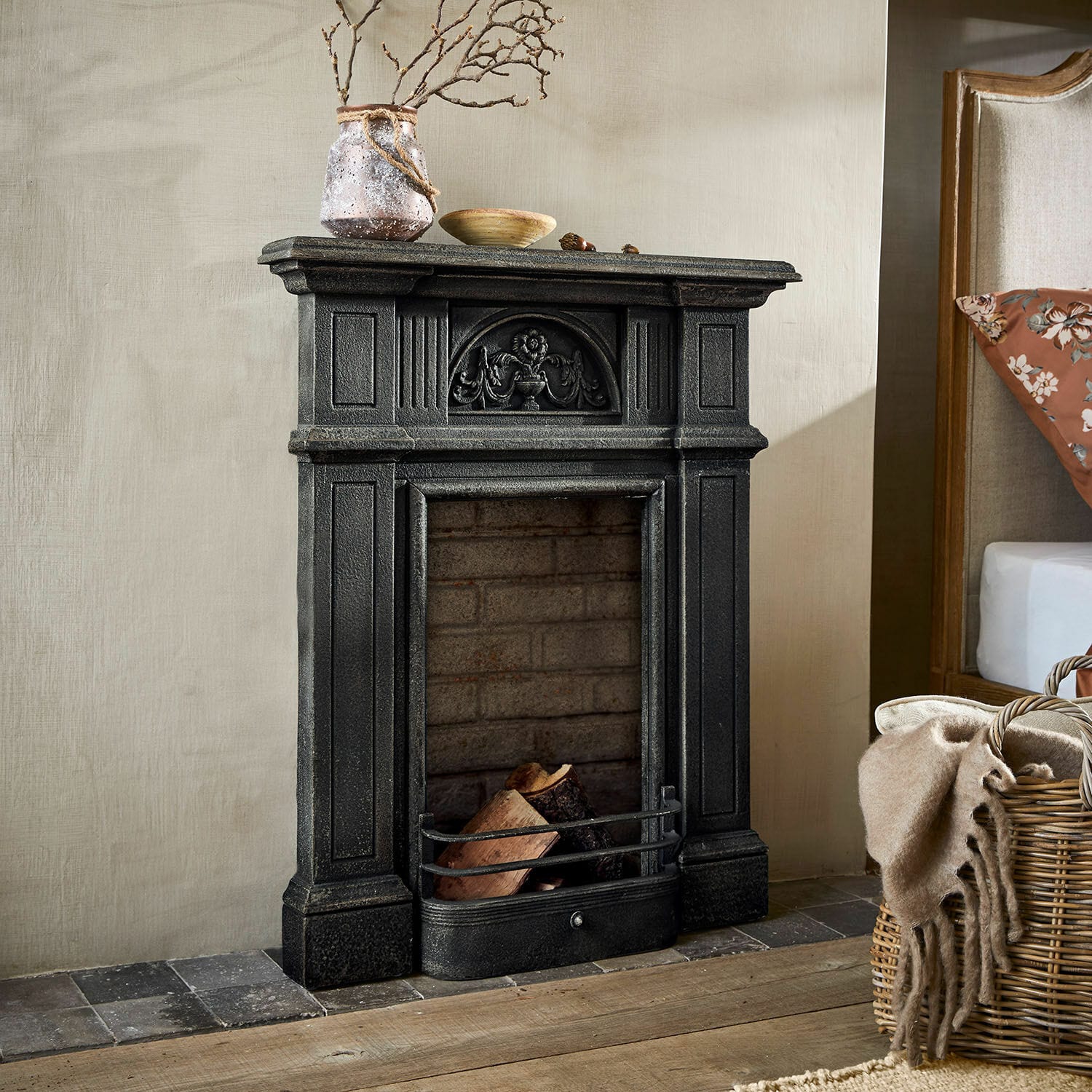 Haardschouw Corvelle Zwarte decoratieve gietijzeren open haard met hout en versieringen in rustieke kamer