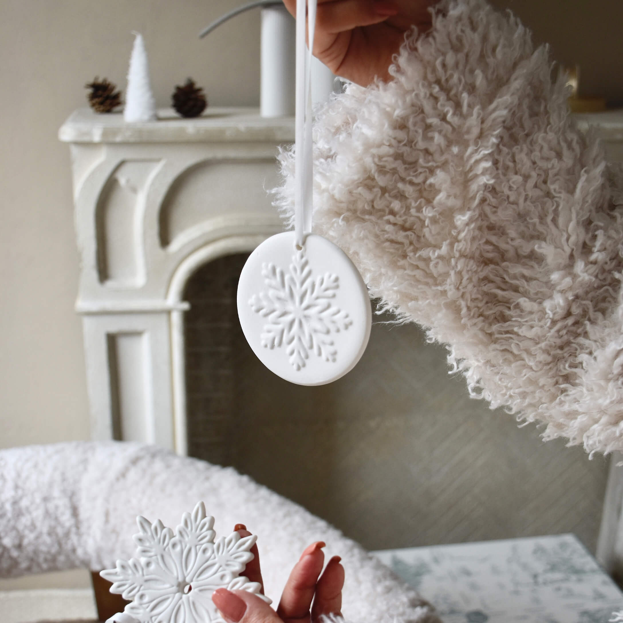 Décorations de Noël en céramique blanche avec motif flocon de neige, tenue devant une cheminée et un pull doux