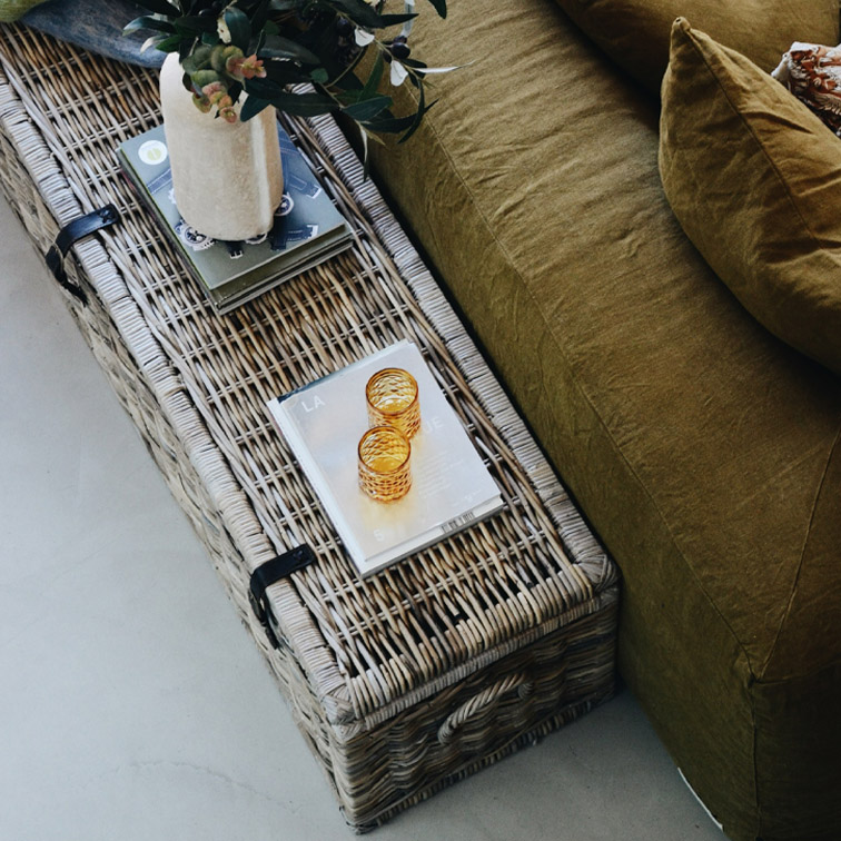 Table basse en rotin naturel avec décorations et canapé vert olive, ambiance cosy et naturelle