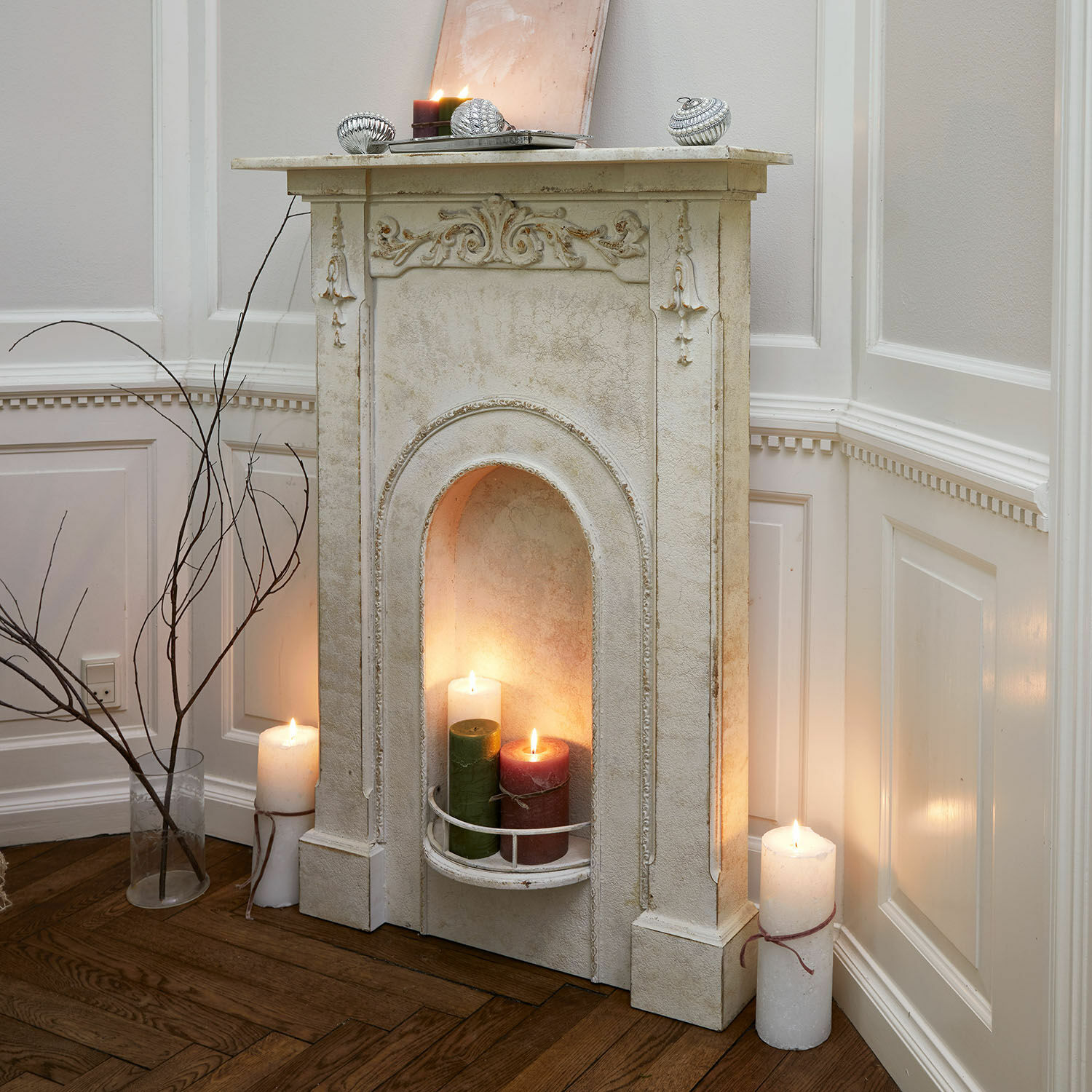 Manteau de cheminée Câlanette Cheminée décorative blanche avec détails sculptés et bougies allumées dans un salon au sol en bois