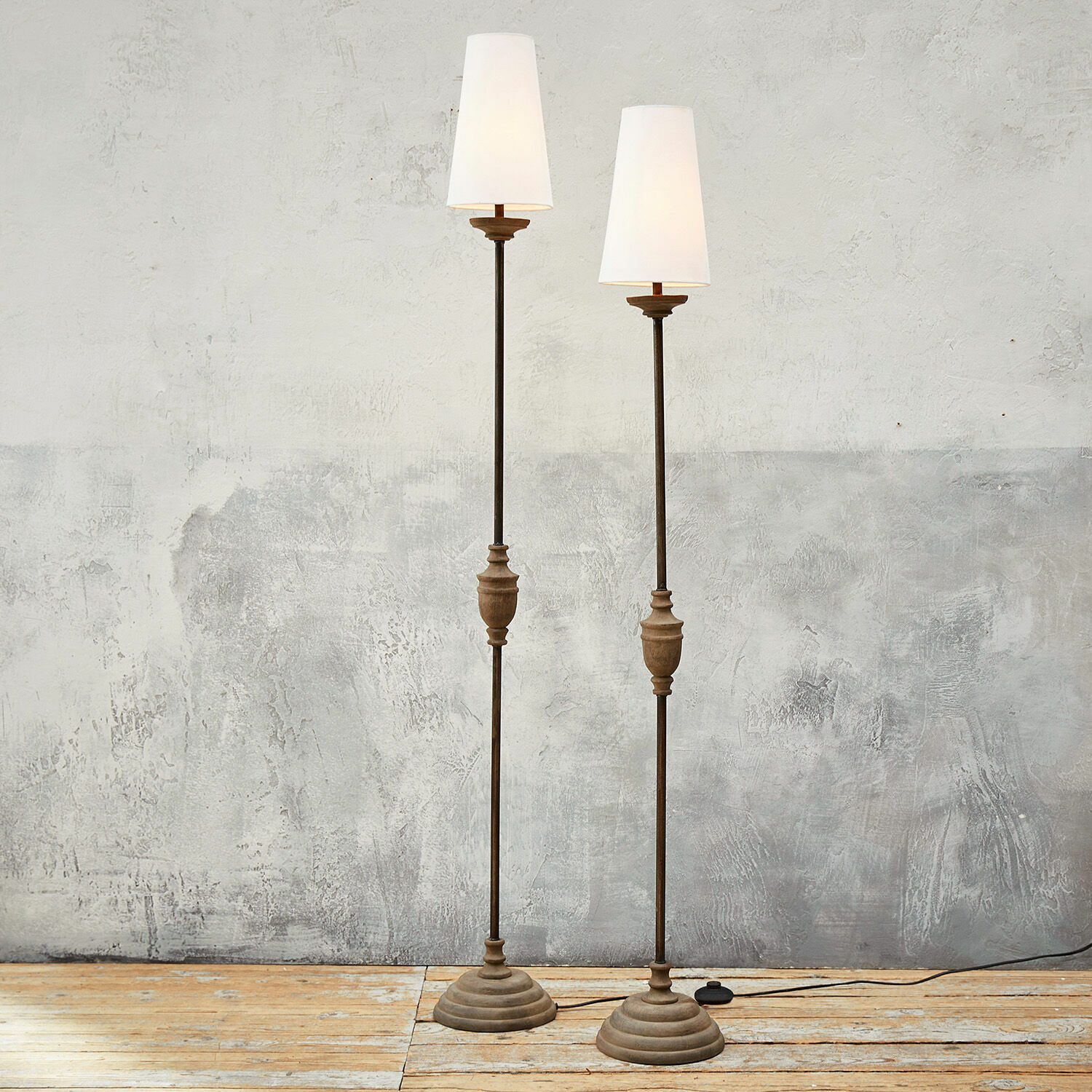 Lot de 2 lampadaires Abigail Deux lampadaires en métal et bois avec abat-jours blancs sur un sol en bois clair