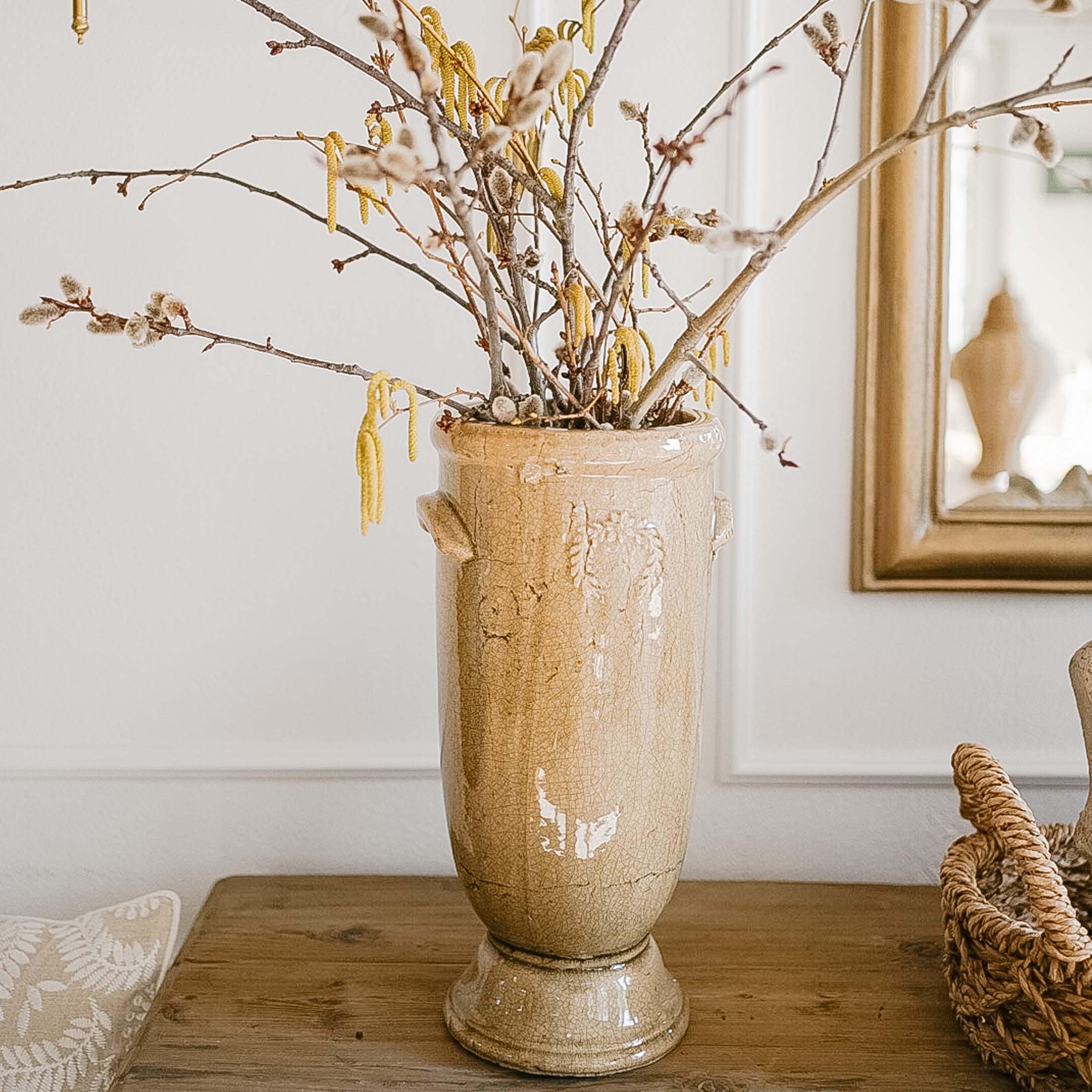 Beige keramische vaas met bloemen en takken op houten tafel in lichte kamer