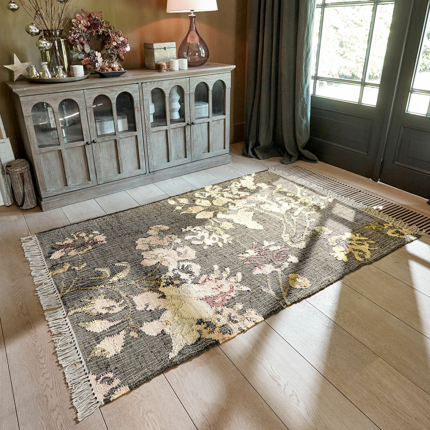 Tapis Yasirah Tapis à motif floral gris et beige sur parquet clair dans un salon lumineux avec meuble en bois