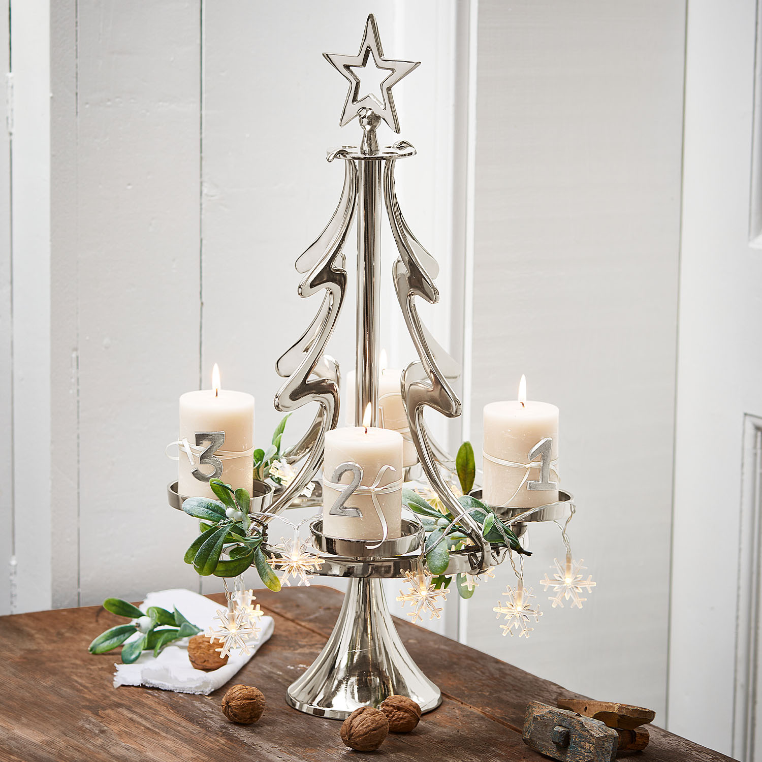 Metalen kandelaar in kerstboomvorm met vier witte kaarsen en kerstdecoratie op houten tafel