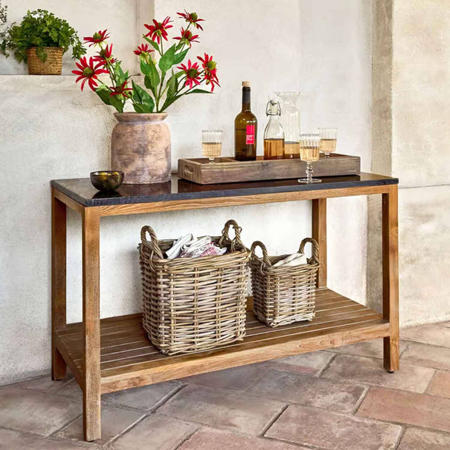 Table en bois avec plateau noir, vase avec fleurs rouges et paniers en osier en dessous dans un intérieur rustique