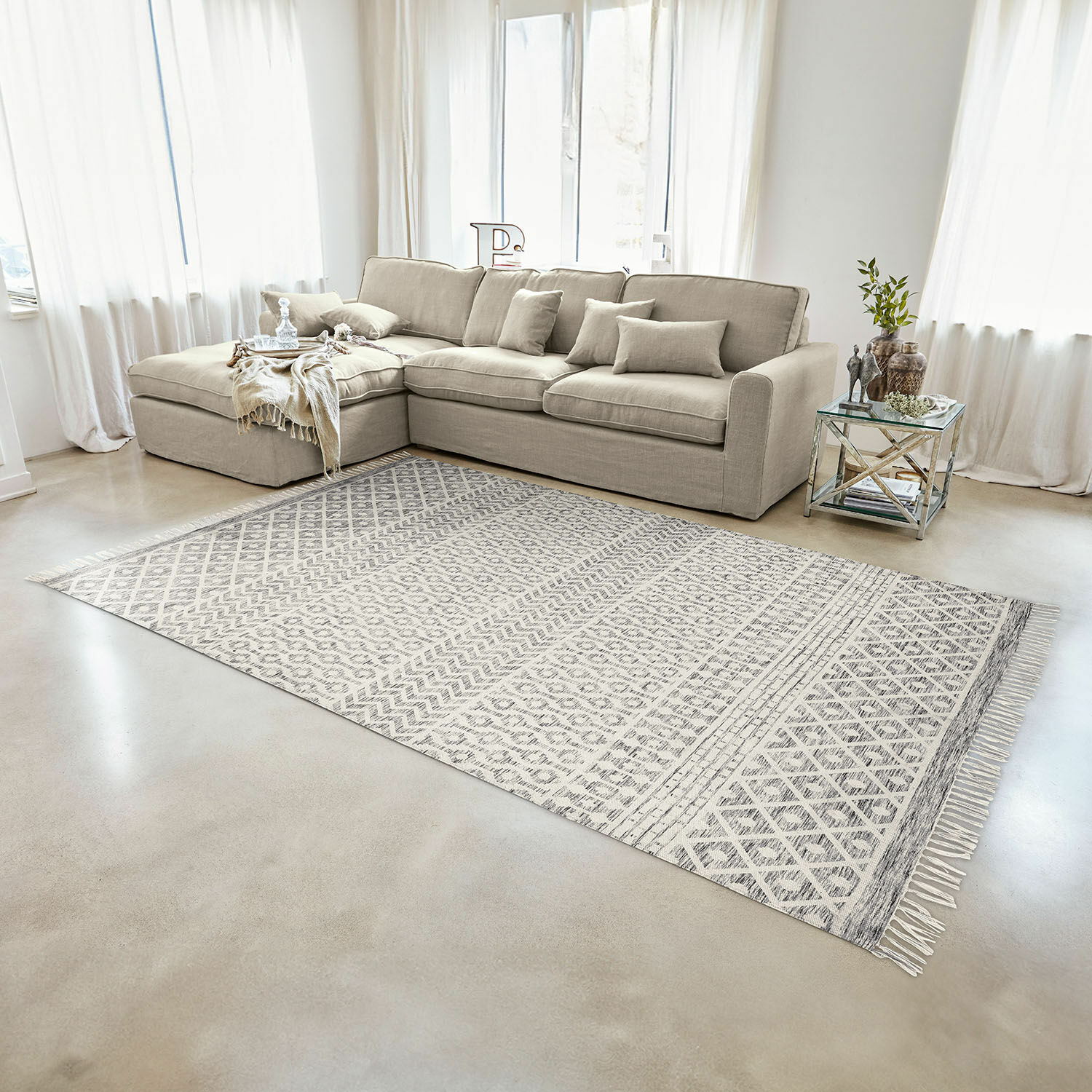 Tapis d'intérieur et d'extérieur Champigny Canapé d'angle beige en tissu dans un salon lumineux avec tapis à motifs géométriques et table en verre