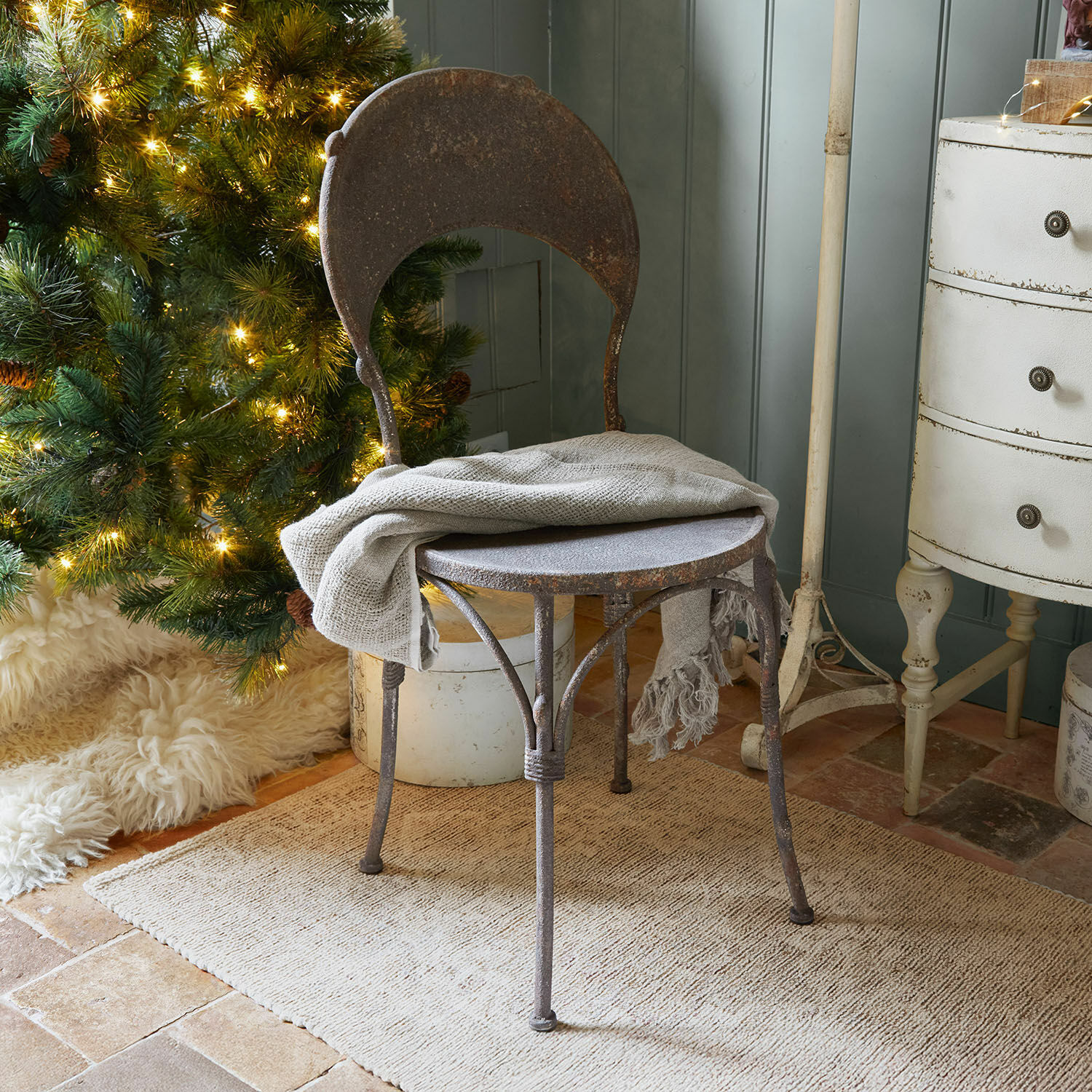 Stoel Delivora Rustieke metalen stoel met roestkleur en grijze deken bij verlichte kerstboom en beige vloerkleed
