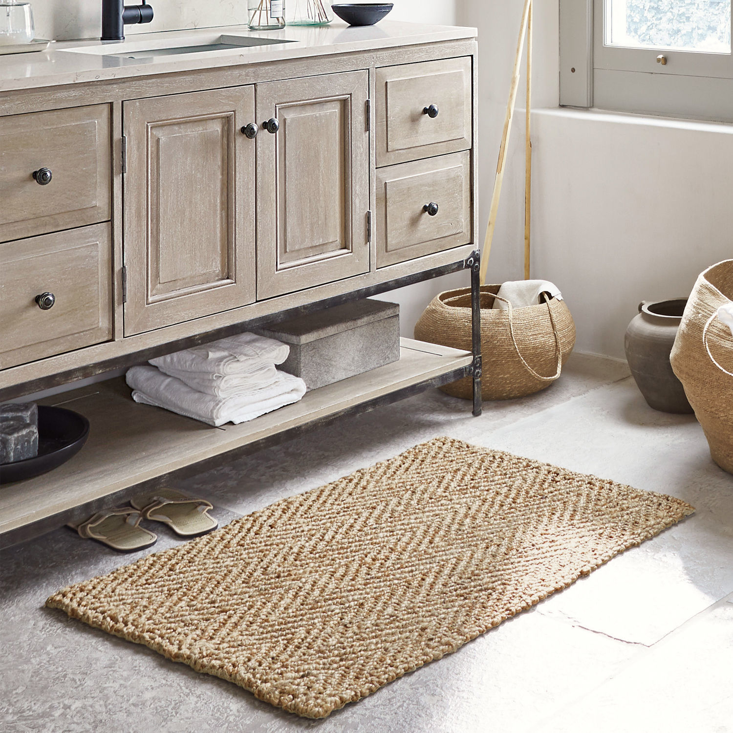 Tapis de bain Daoukro Tapis beige en jute à motif chevron dans une salle de bain avec meuble en bois et paniers tressés