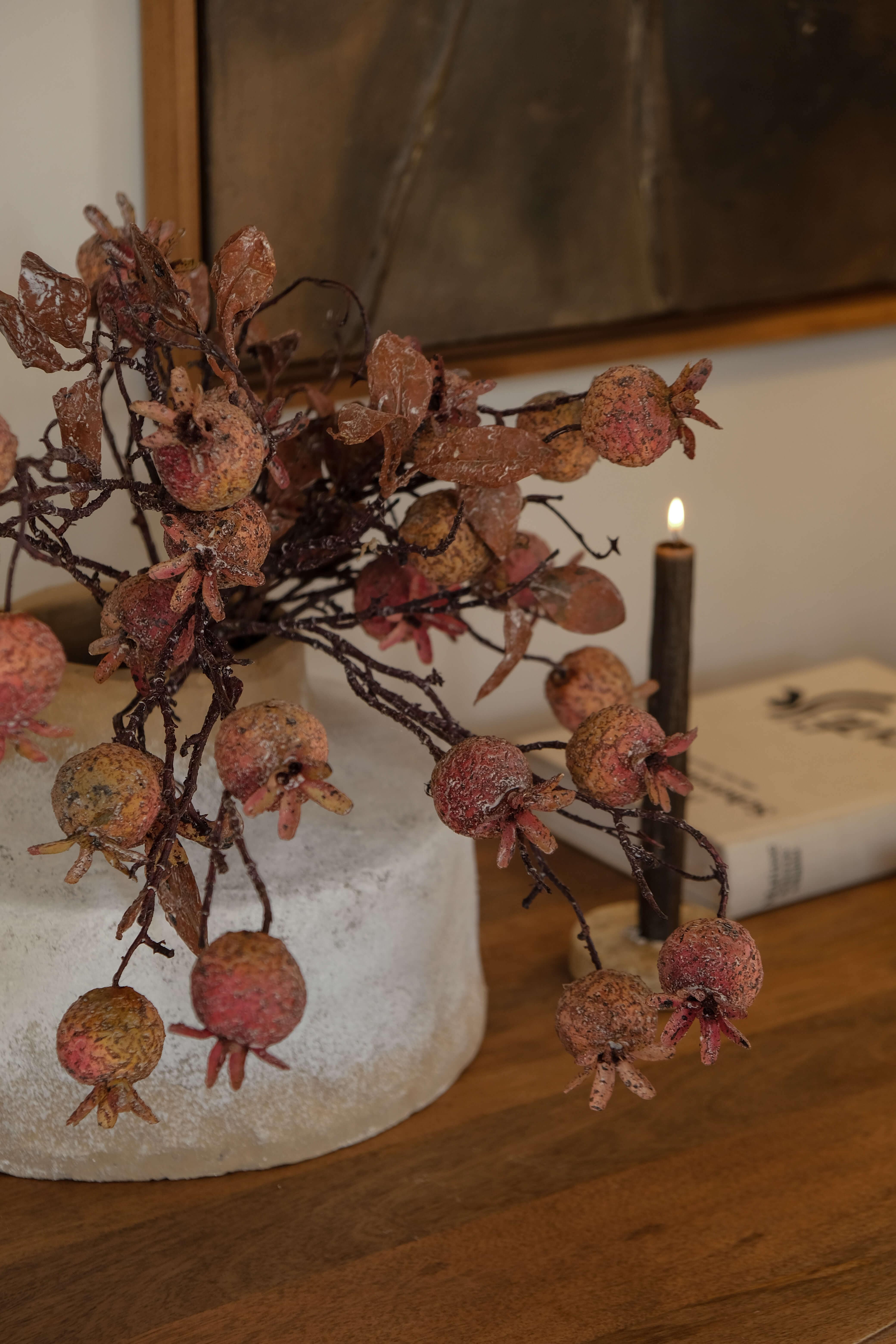 Decoratieve tak met granaatappelvruchten in natuurlijke tinten op lichte voet op houten tafel