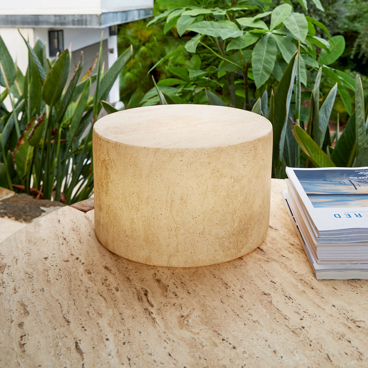 Oplaadbare ledlamp Marévos Ronde bijzettafel van beige travertijn op terras met groene planten, natuursteen