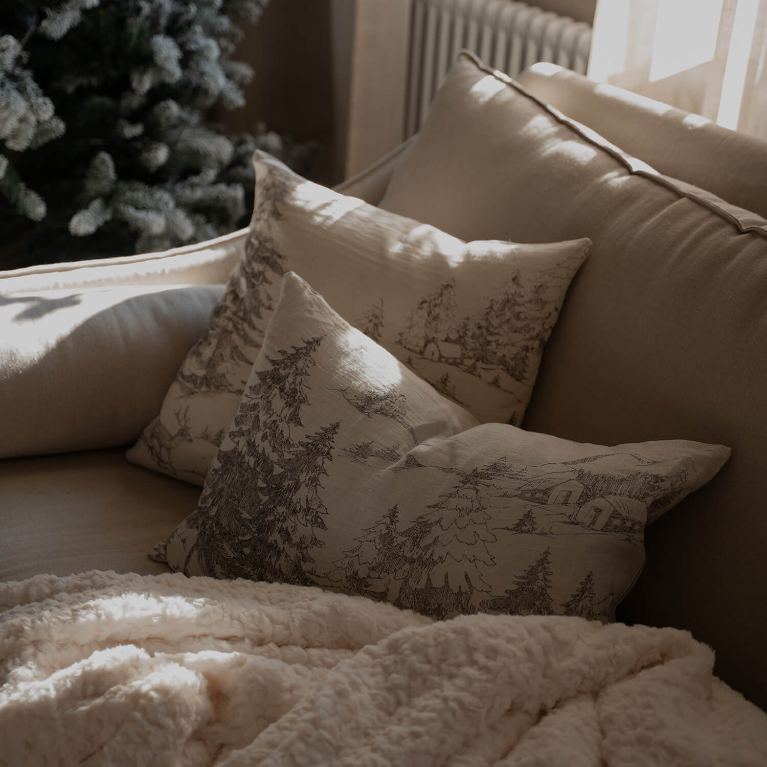 Canapé beige avec coussins décoratifs à motif forêt et couverture douce crème pour salon cosy