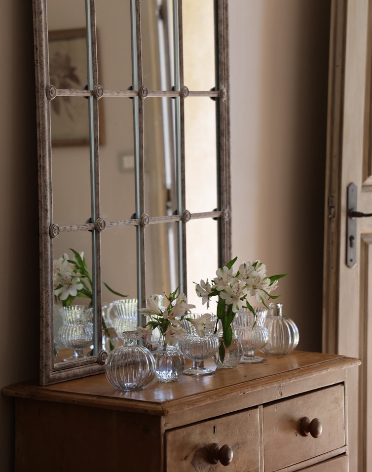 Commode en bois rustique avec miroir à cadre métallique et vases en verre avec fleurs blanches