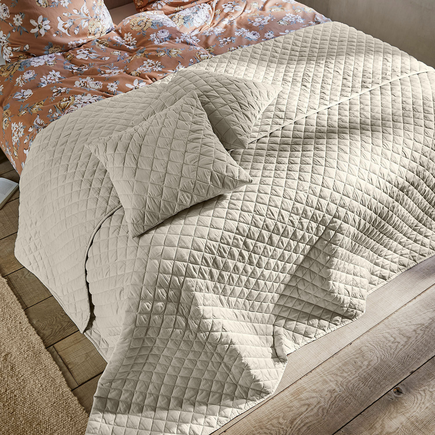 Quilt Jolique Beige gewatteerde bedsprei en kussens op bed met houten vloer en bloemenbedlinnen
