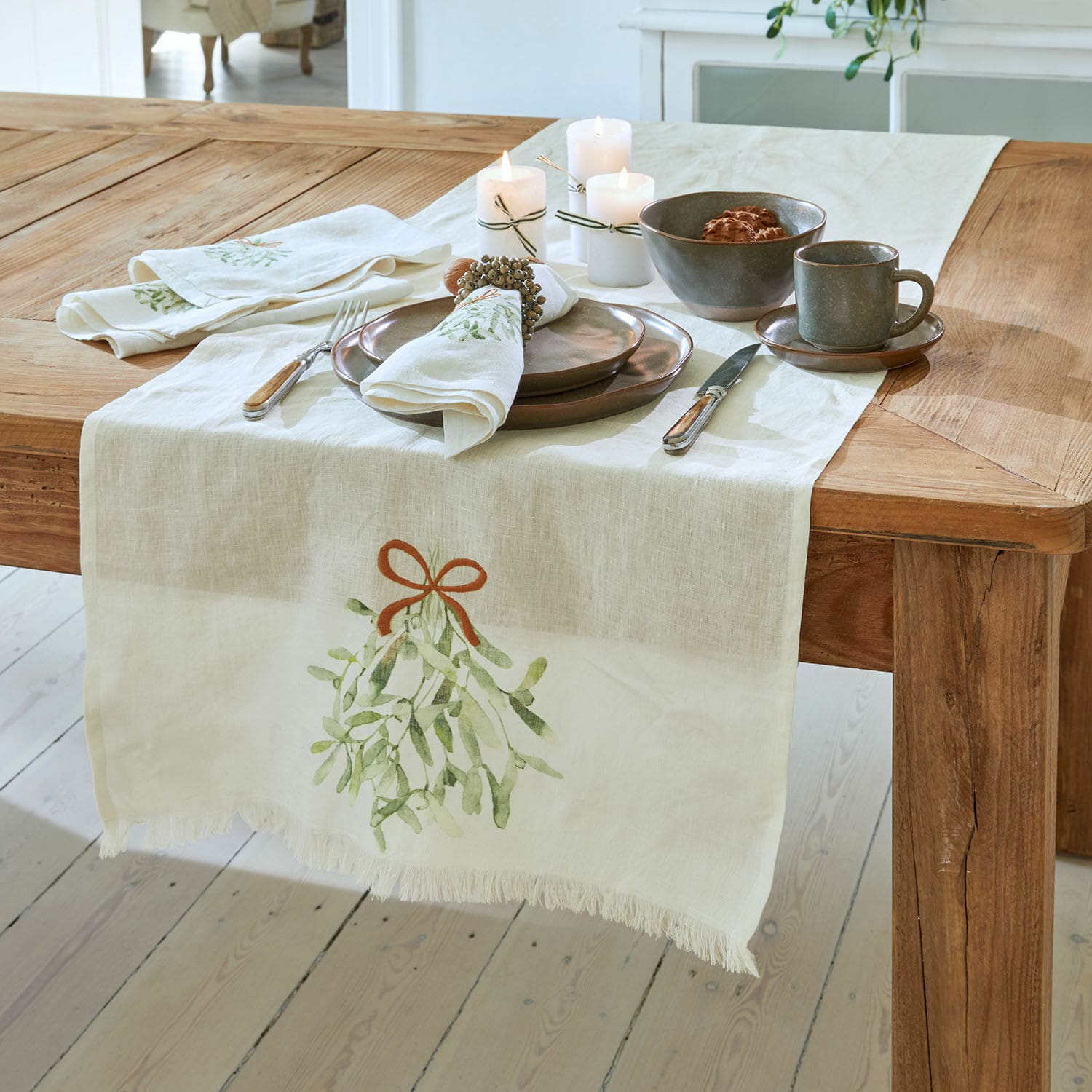 Chemin de table Mistletoe Chemin de table en lin avec motif de gui sur table en bois et vaisselle rustique