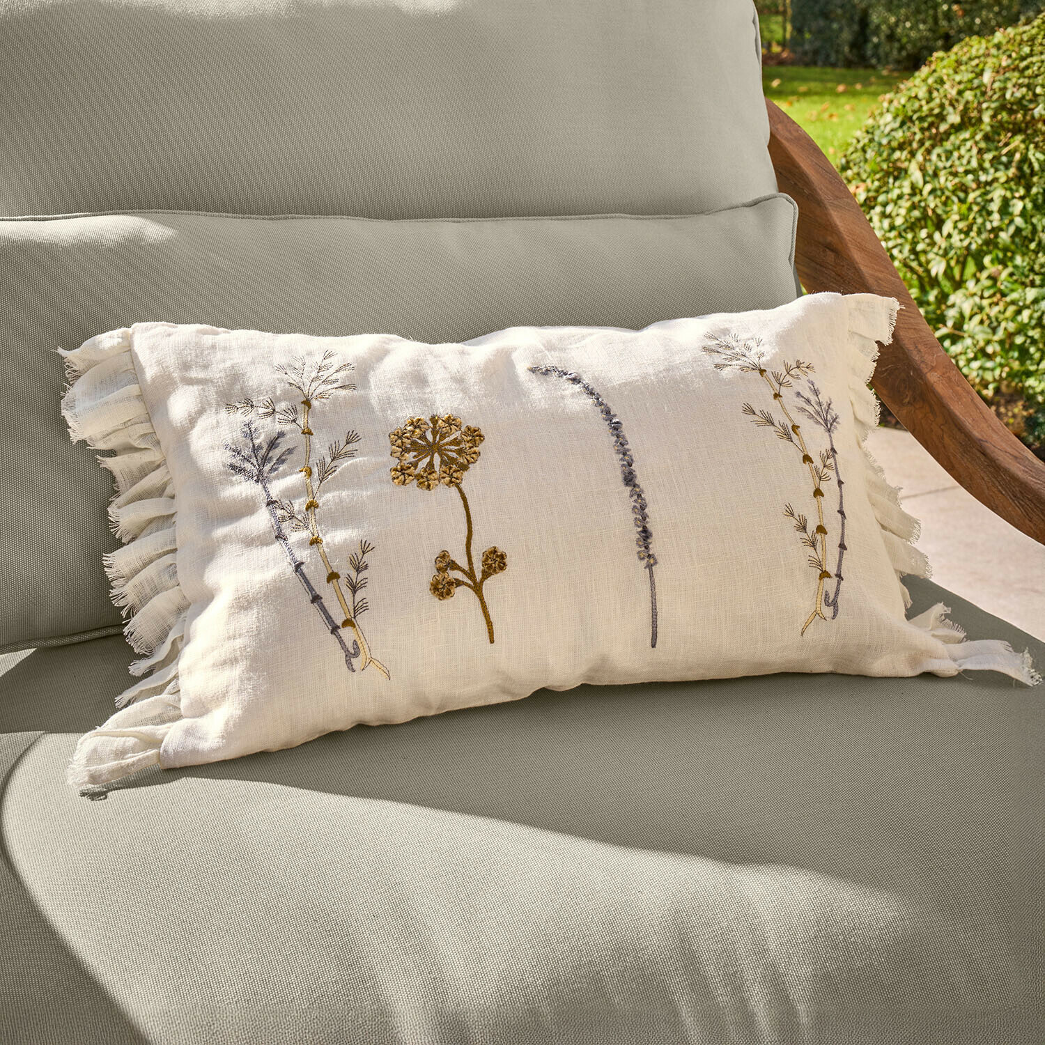 Housse de coussin Quélivane Coussin beige en lin avec broderies florales et franges sur fauteuil de jardin vert