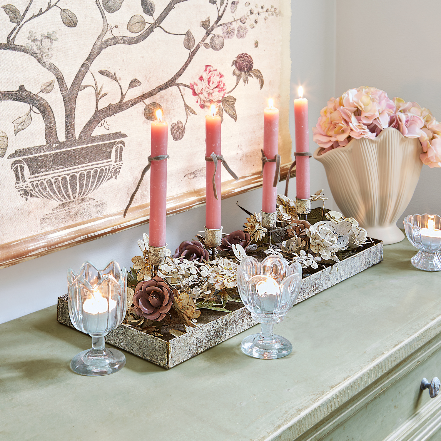 Bougeoir décoratif en métal avec fleurs et bougies roses sur commode verte avec vase à fleurs