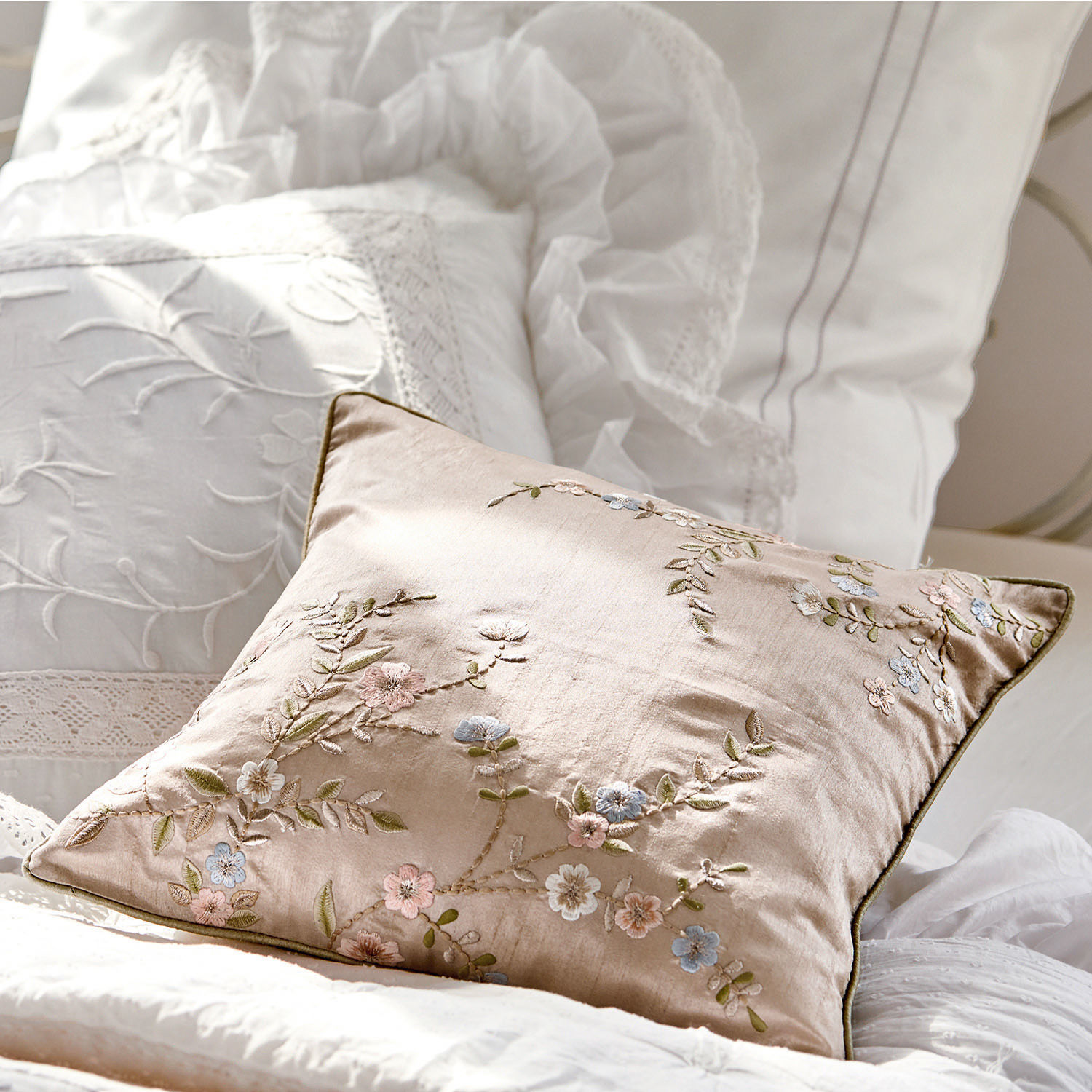 Beige sierkussen met geborduurde bloemen op wit beddengoed, zachte stof