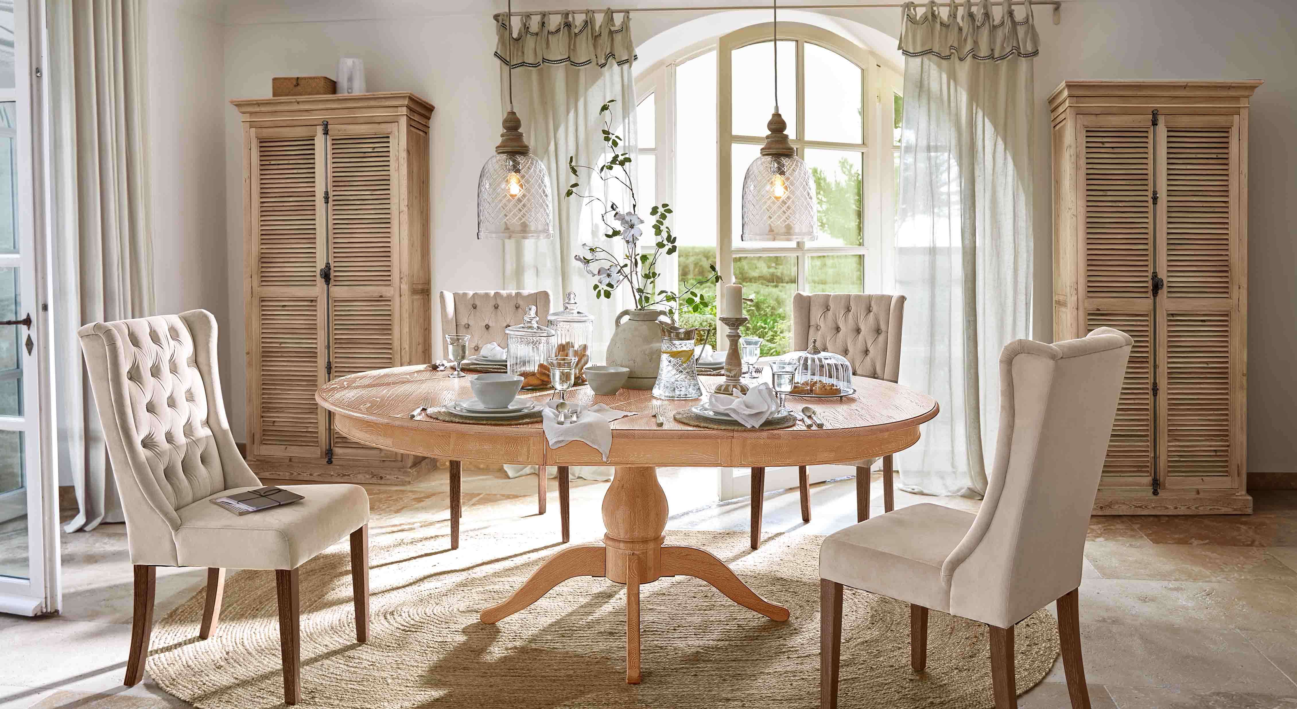 Salle à manger avec table ronde en bois clair et chaises rembourrées beige dans un style classique