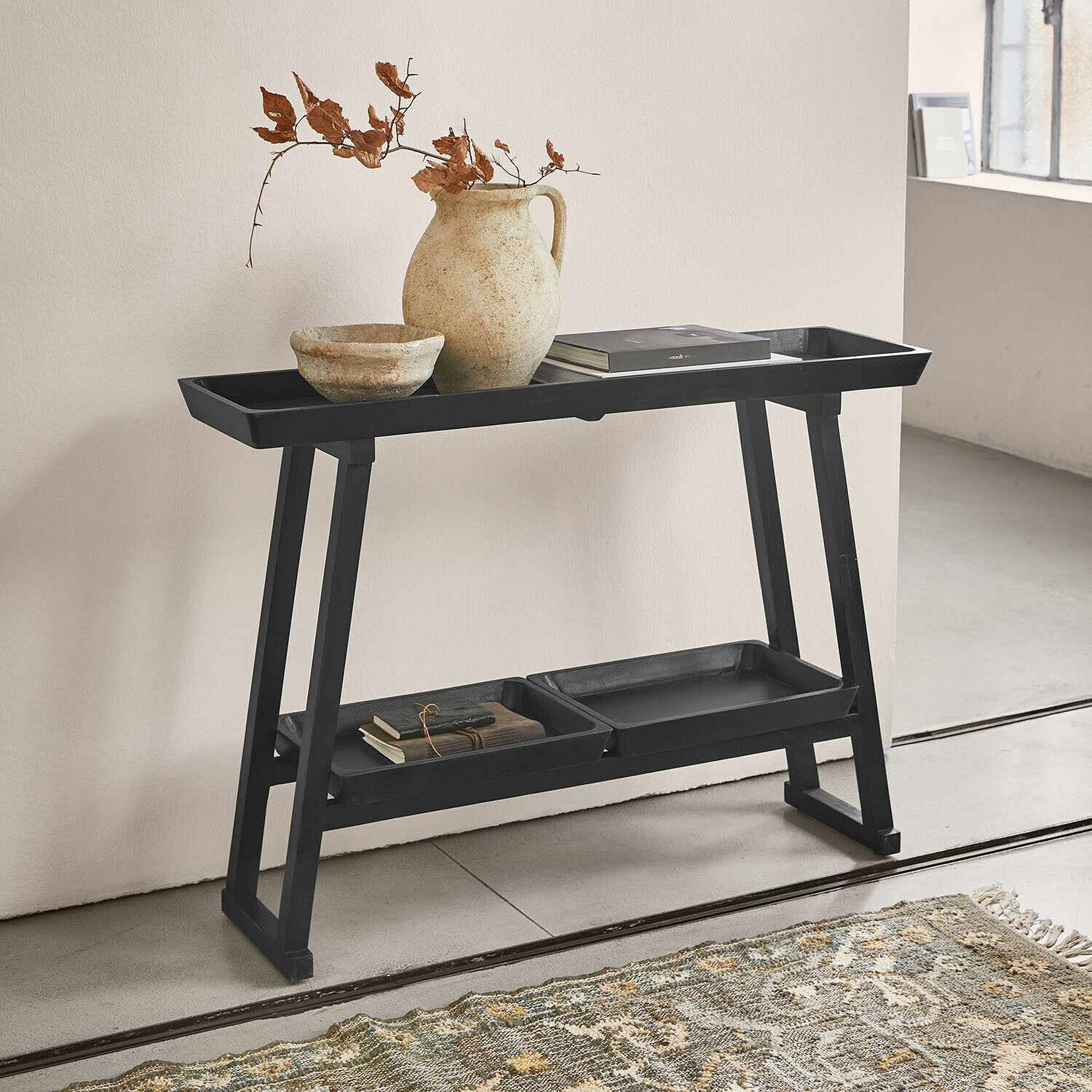 Zwart houten bijzettafeltje met planken, keramische vaas en boeken in minimalistisch interieur