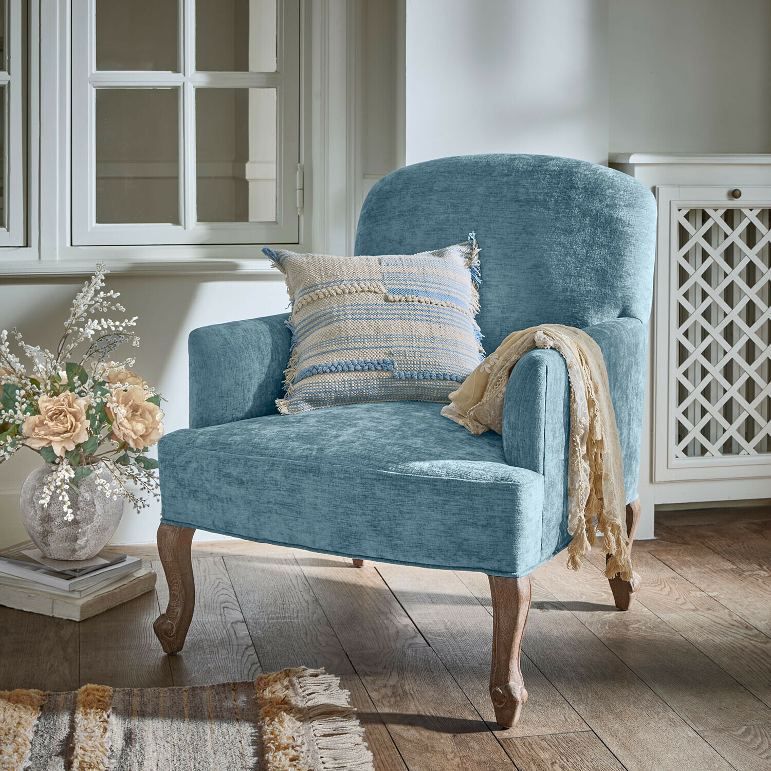 Fauteuil Clairmont Bleu Blauwe gestoffeerde fauteuil met houten poten en decoratief kussen in een gezellige kamer