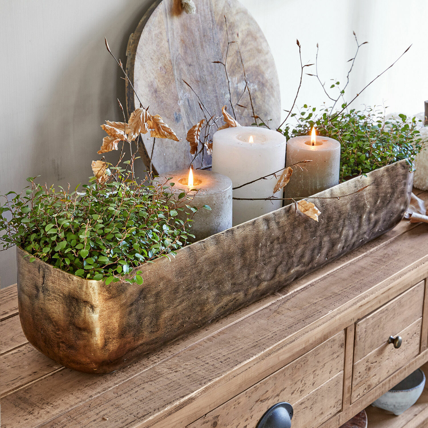 Schaal Skye Decoratieve gouden metalen plantenbak met groene planten en drie kaarsen op houten tafel